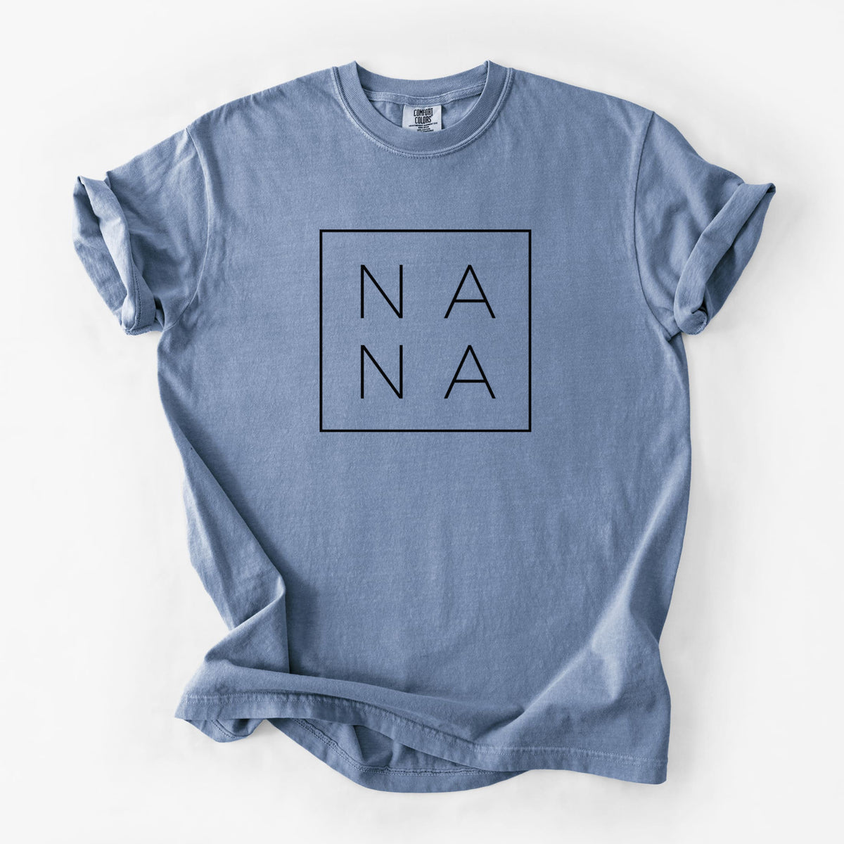 Blue jean Comfort Colors t-shirt laid flat, printed with the word NANA in thin black letters stacked inside a square outline.