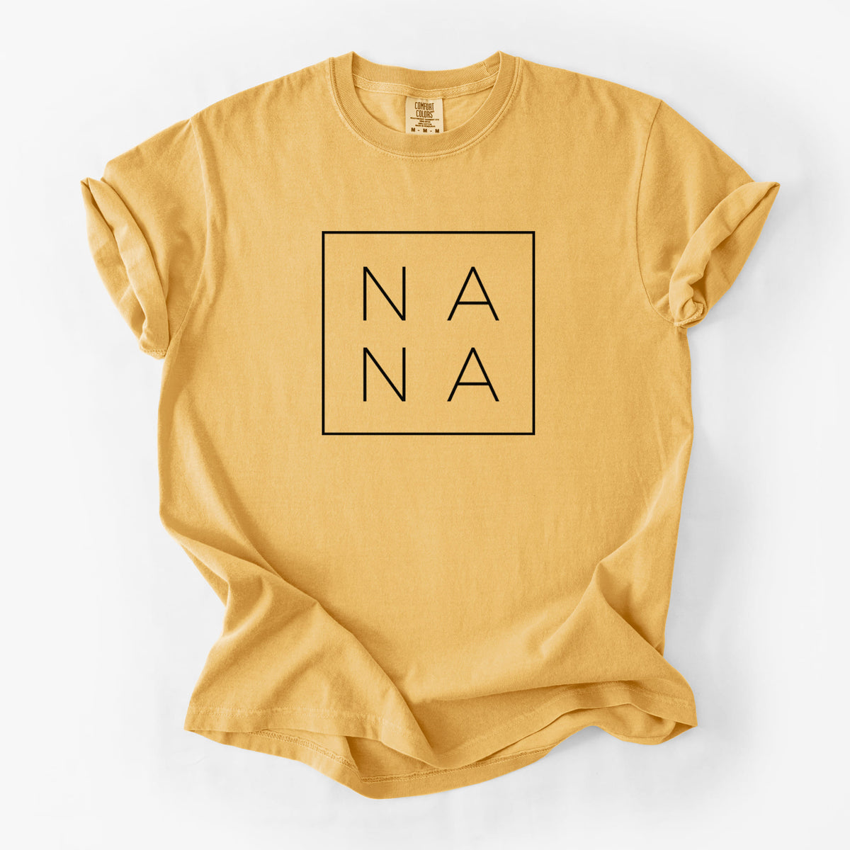Golden wheat yellow Comfort Colors t-shirt laid flat, printed with the word NANA in thin black letters stacked inside a square outline.