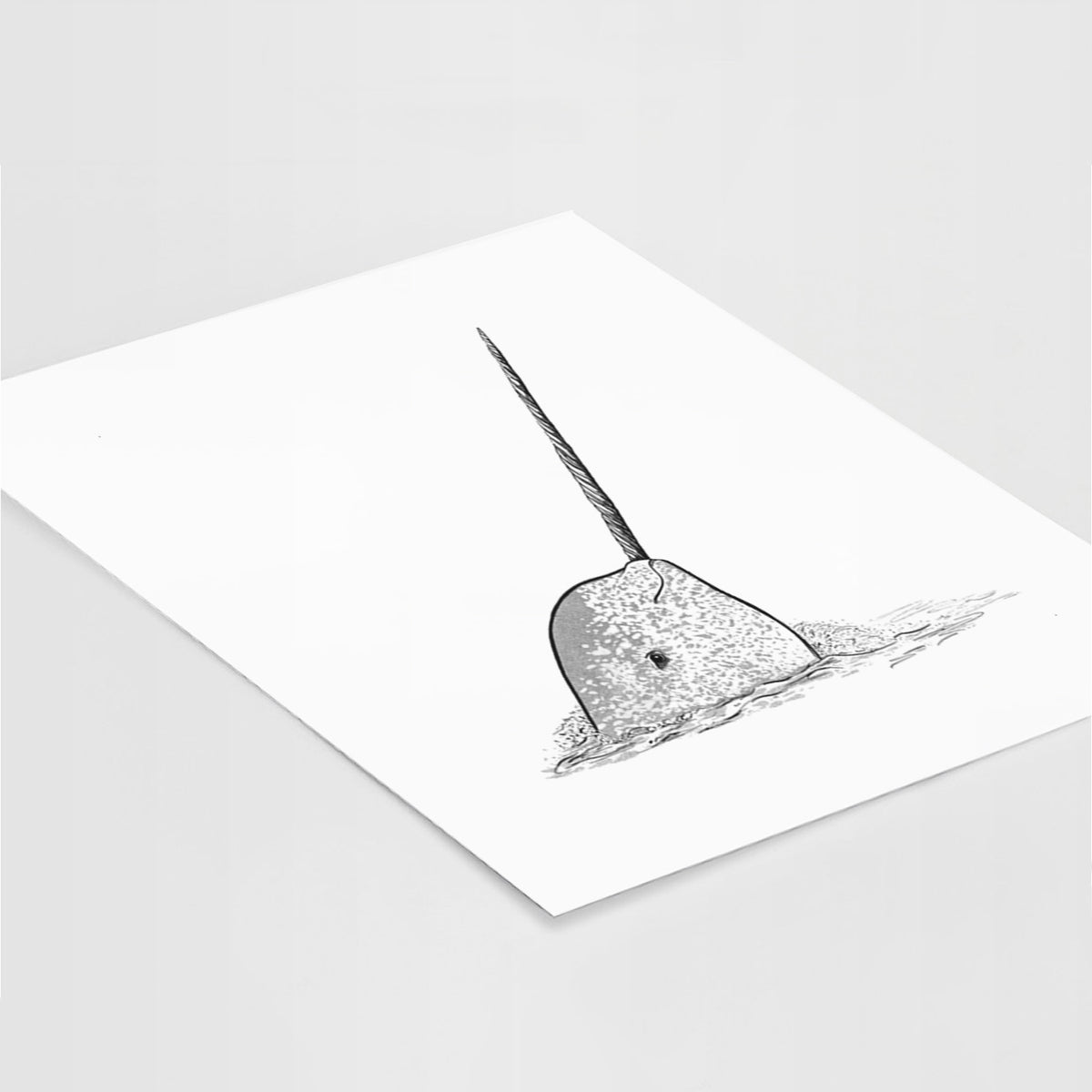 Art print of a black ink illustration of a narwhal with its long spiral tusk pointing upward, lying at an angle on a white surface.