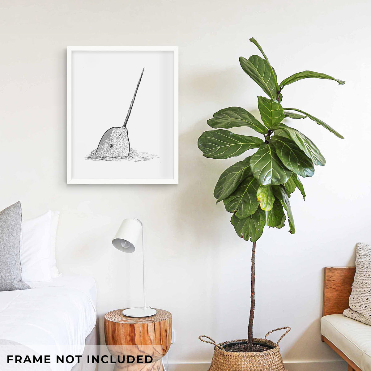 Art print of a black ink illustration of a narwhal with its long spiral tusk pointing upward, shown framed on a living room wall beside a potted plant. Frame not included.