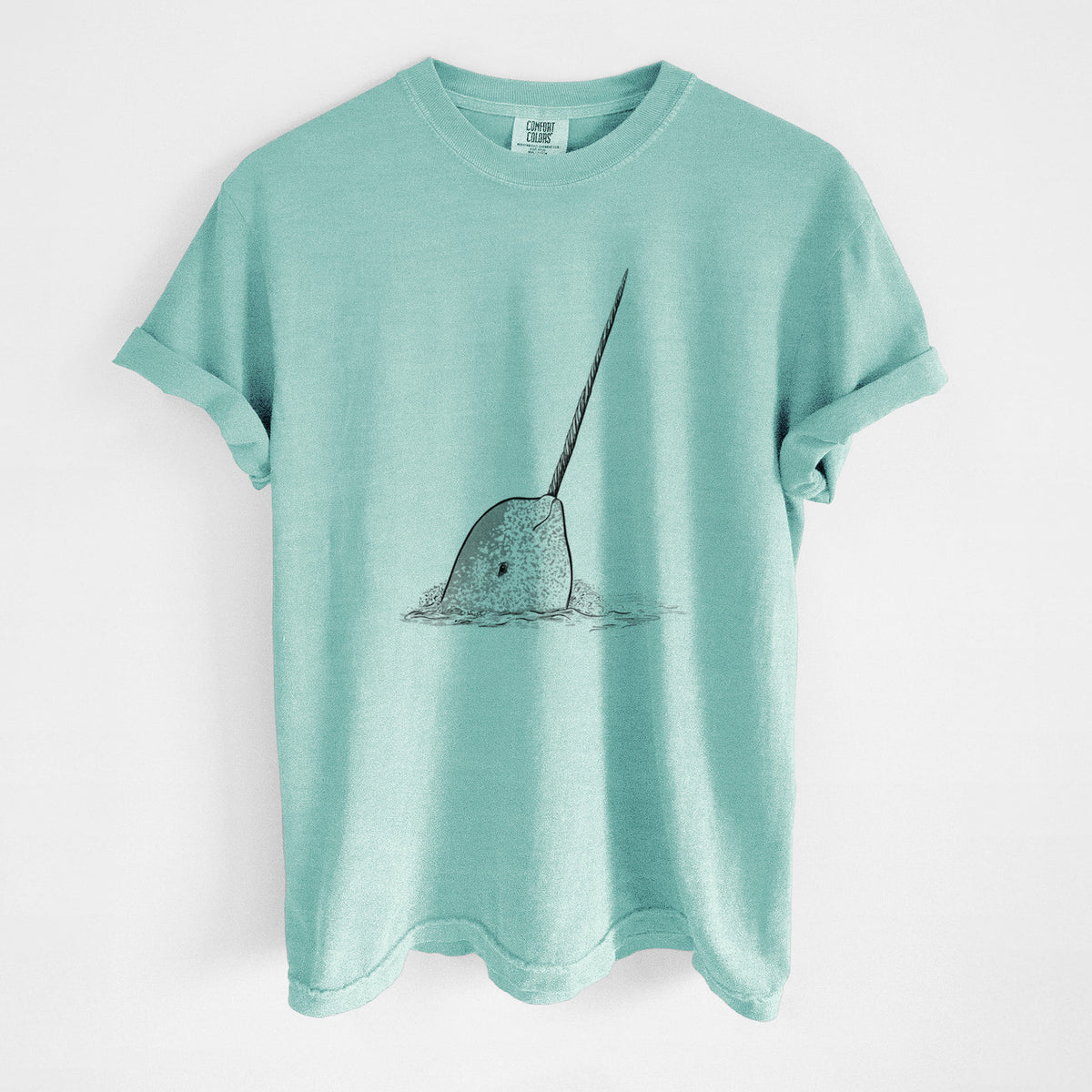 Chalky mint Comfort Colors t-shirt laid flat, printed with a black ink illustration of a narwhal with its long spiral tusk pointing upward.
