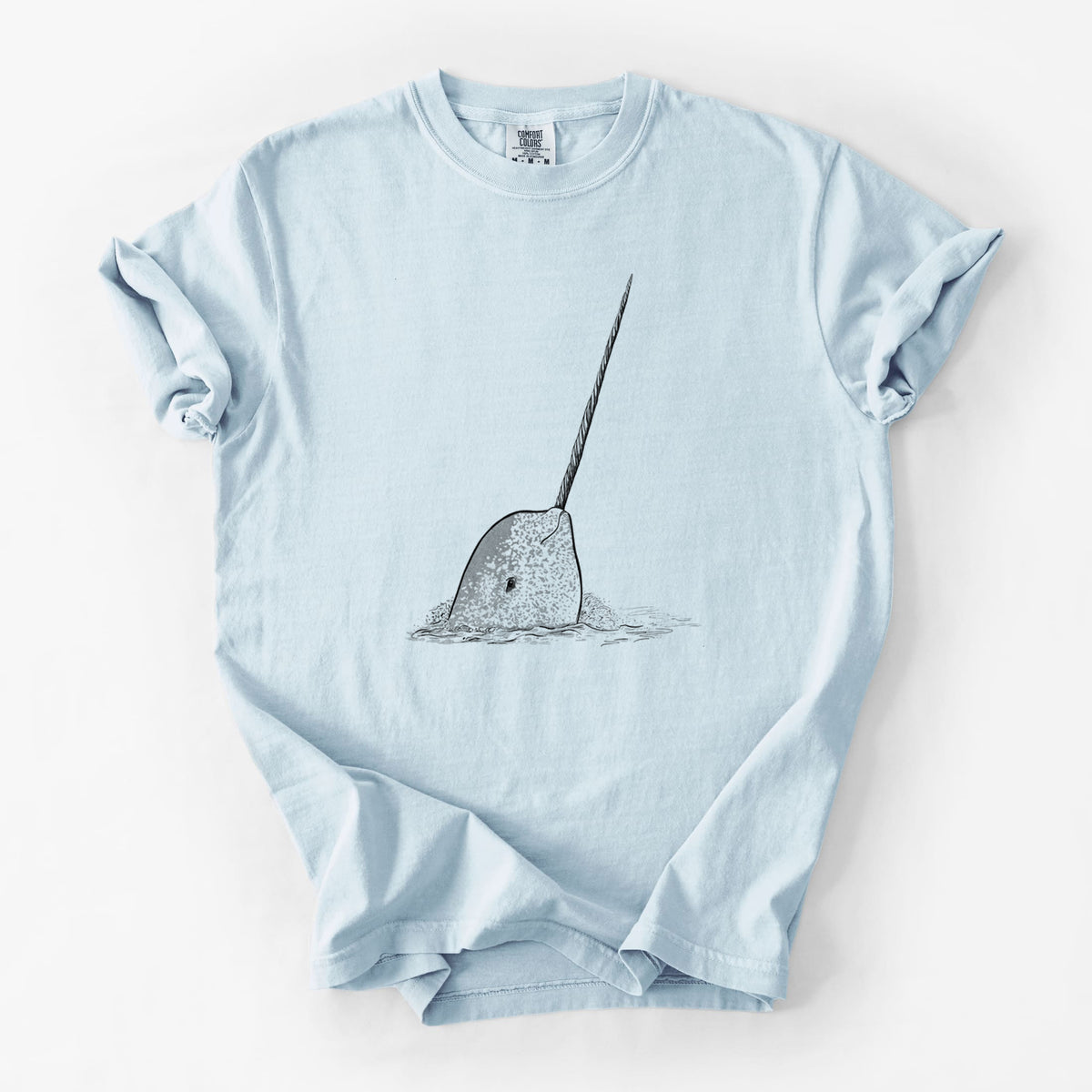 Chambray blue Comfort Colors t-shirt laid flat, printed with a black ink illustration of a narwhal with its long spiral tusk pointing upward.