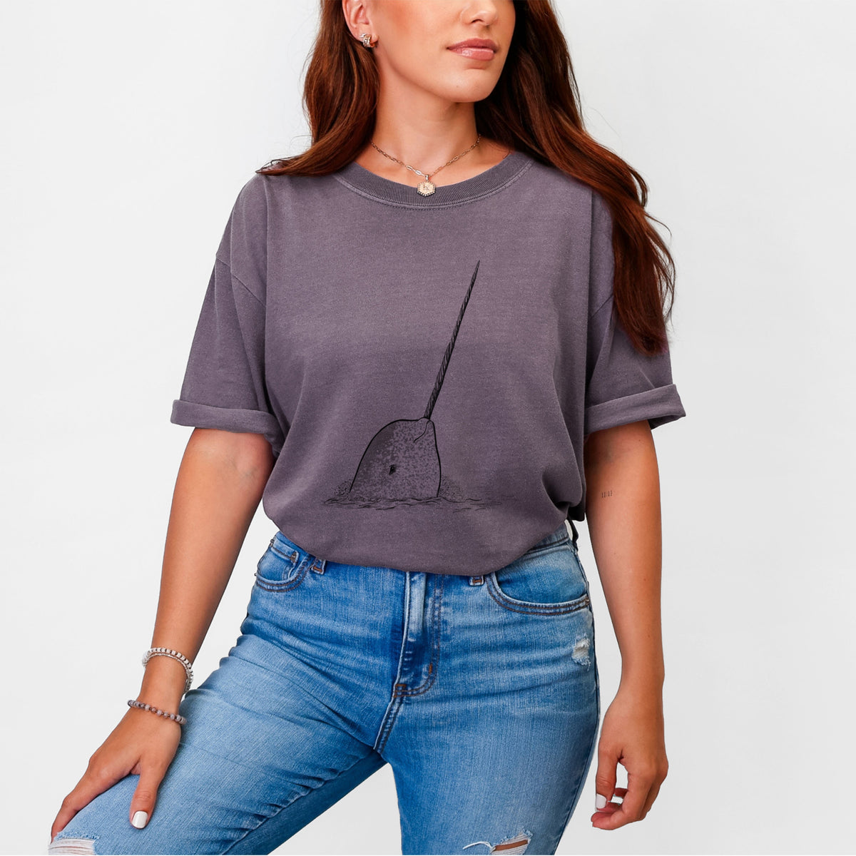 Woman wearing a Comfort Colors t-shirt printed with a black ink illustration of a narwhal with its long spiral tusk pointing upward.