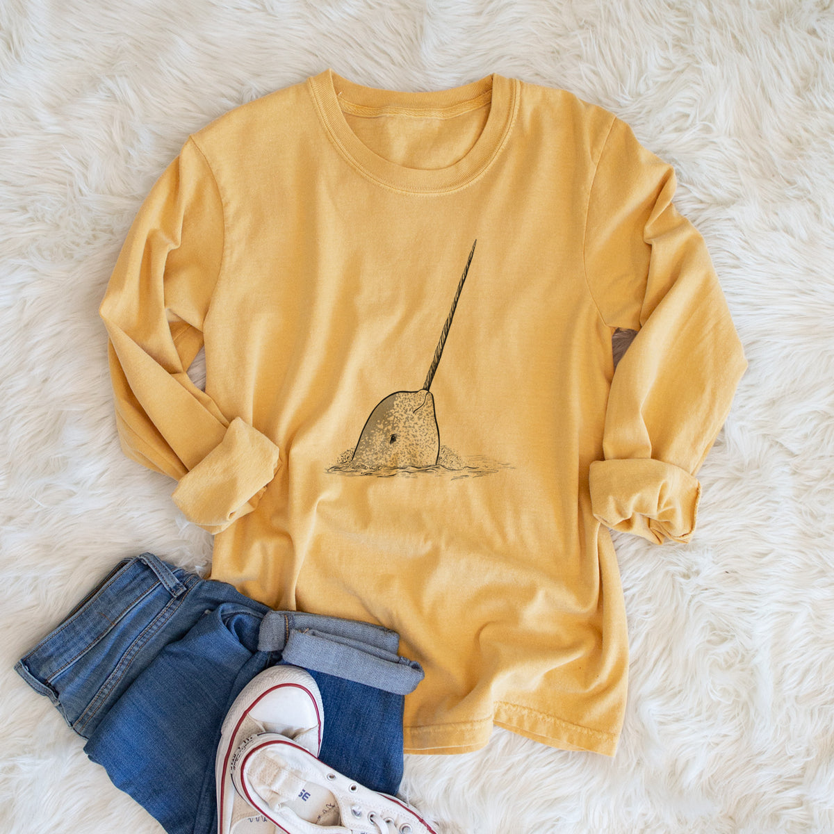 Golden wheat yellow Comfort Colors long sleeve shirt printed with a black ink illustration of a narwhal with its long spiral tusk pointing upward, shown in a lifestyle photo.