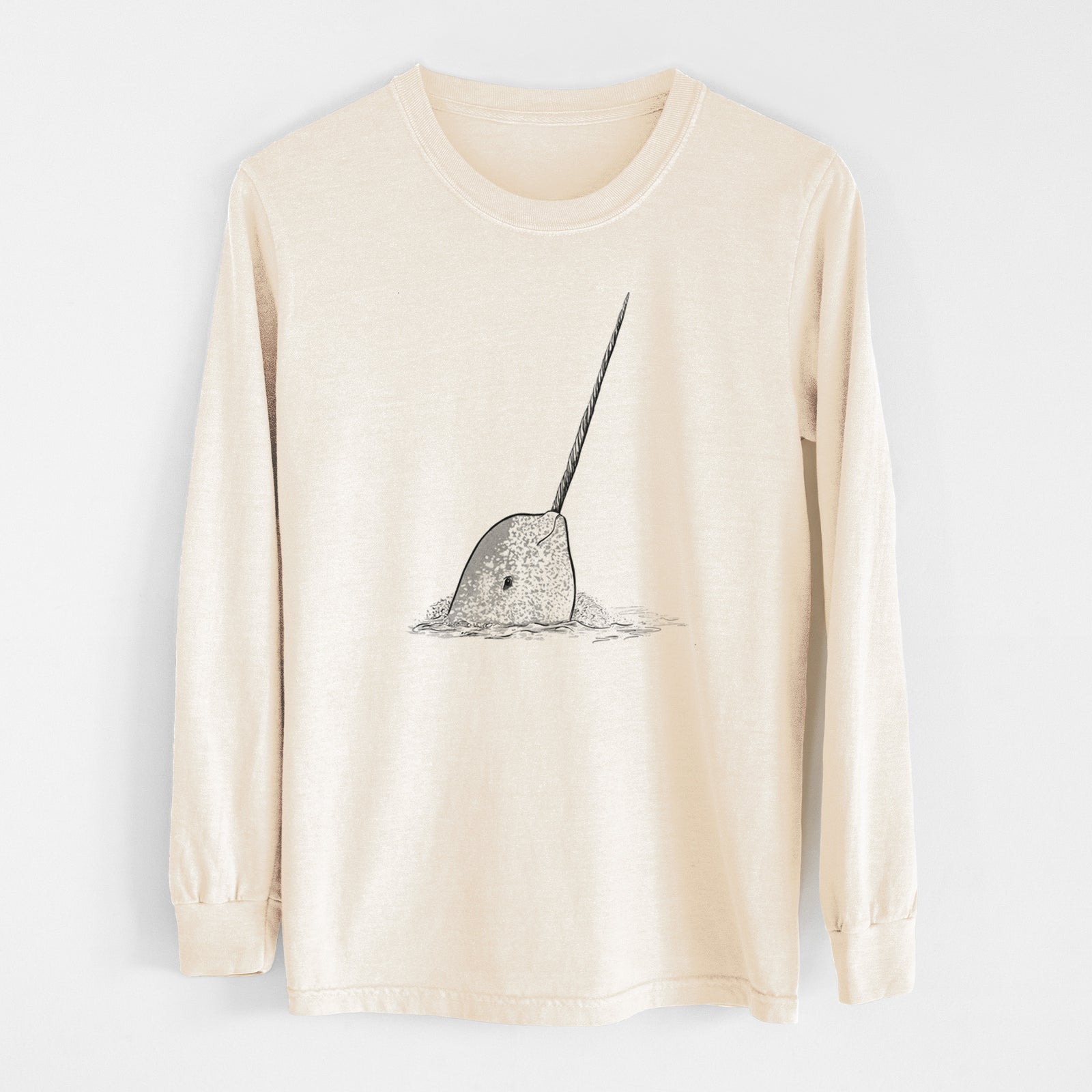 Ivory Comfort Colors long sleeve shirt laid flat, printed with a black ink illustration of a narwhal with its long spiral tusk pointing upward.