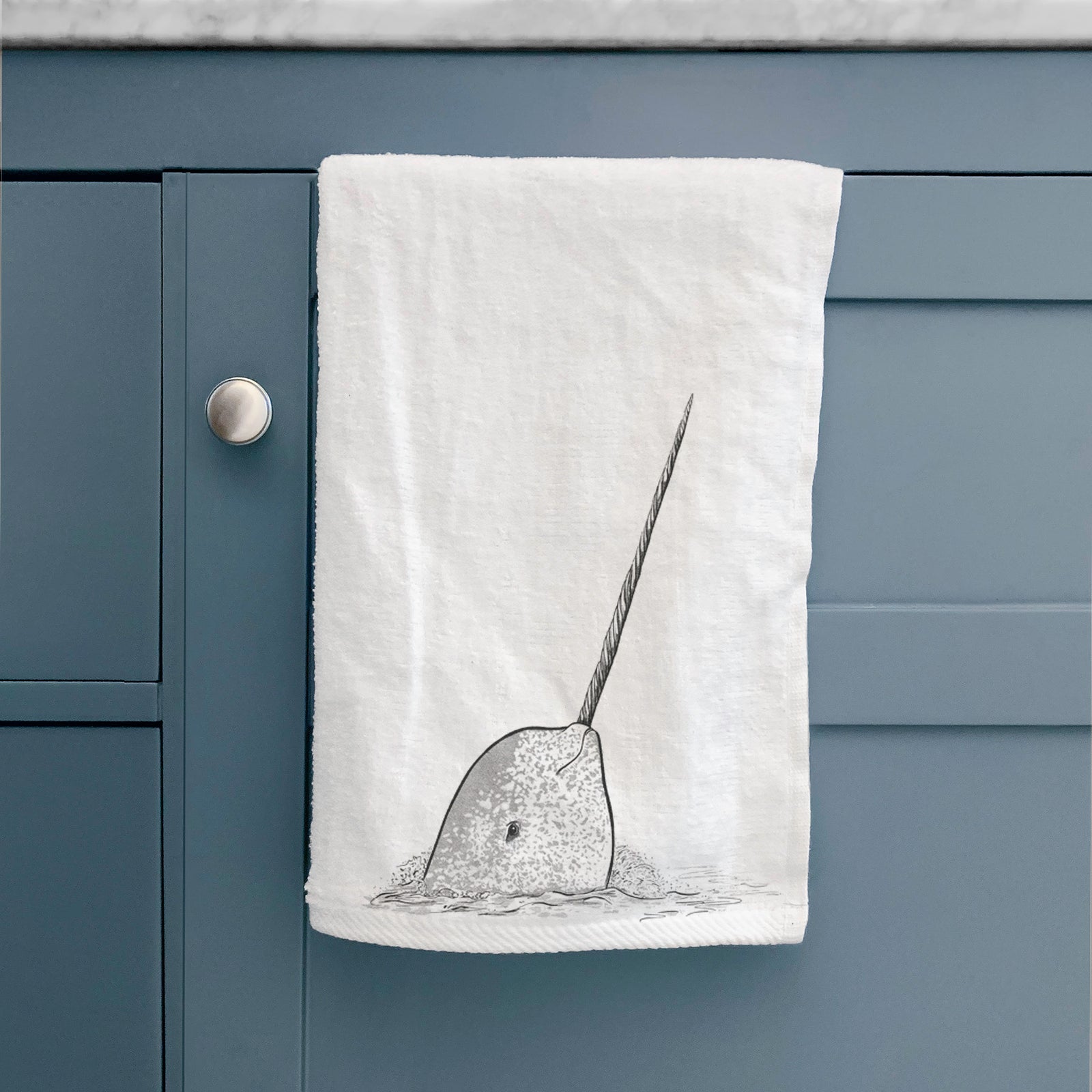 White hand towel printed with a black ink illustration of a narwhal with its long spiral tusk pointing upward.