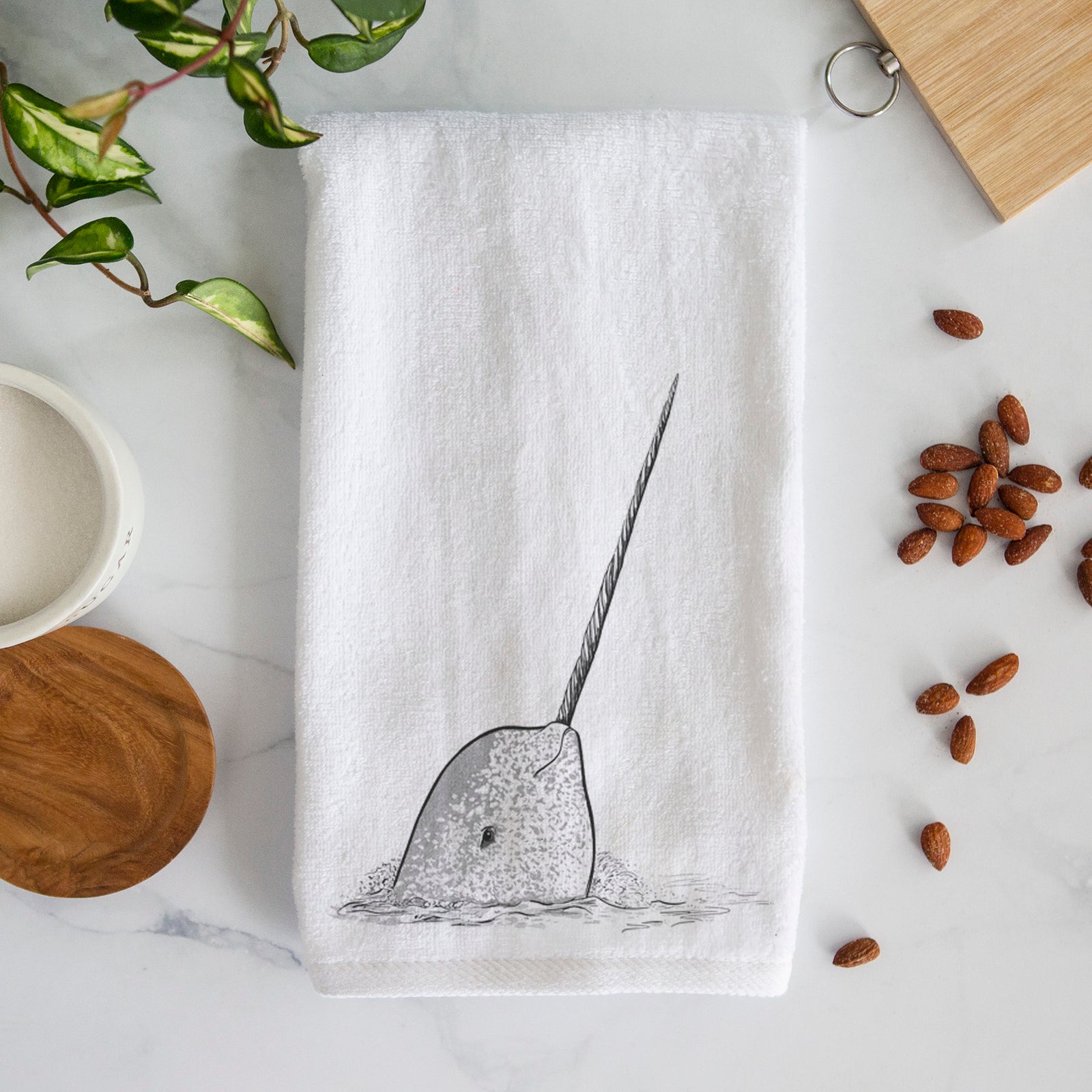 White hand towel printed with a black ink illustration of a narwhal with its long spiral tusk pointing upward.