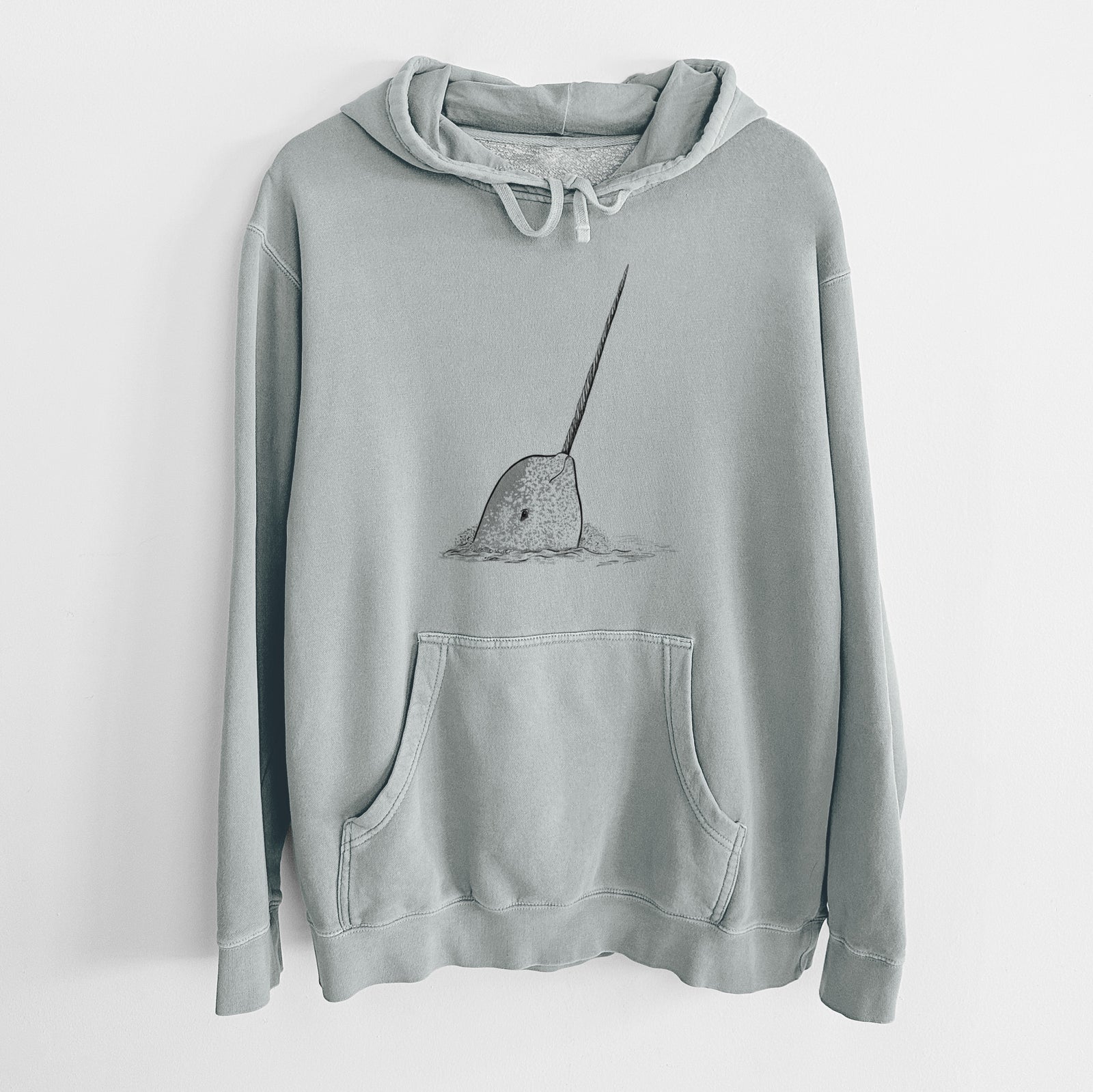 Sage green pigment dyed hoodie laid flat, printed with a black ink illustration of a narwhal with its long spiral tusk pointing upward.