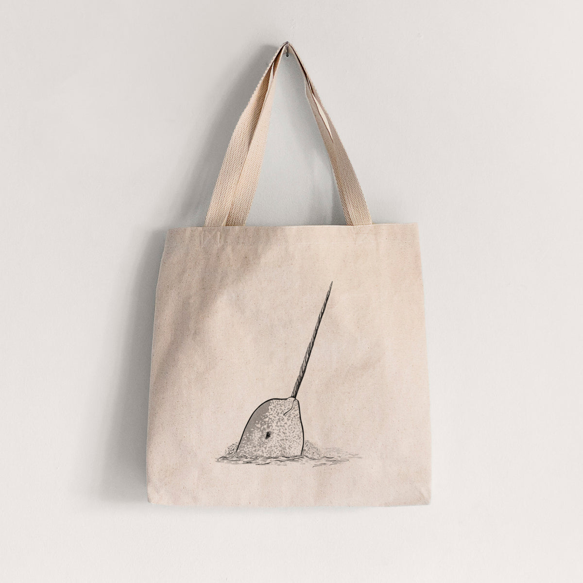 Natural canvas tote bag printed with a black ink illustration of a narwhal with its long spiral tusk pointing upward.