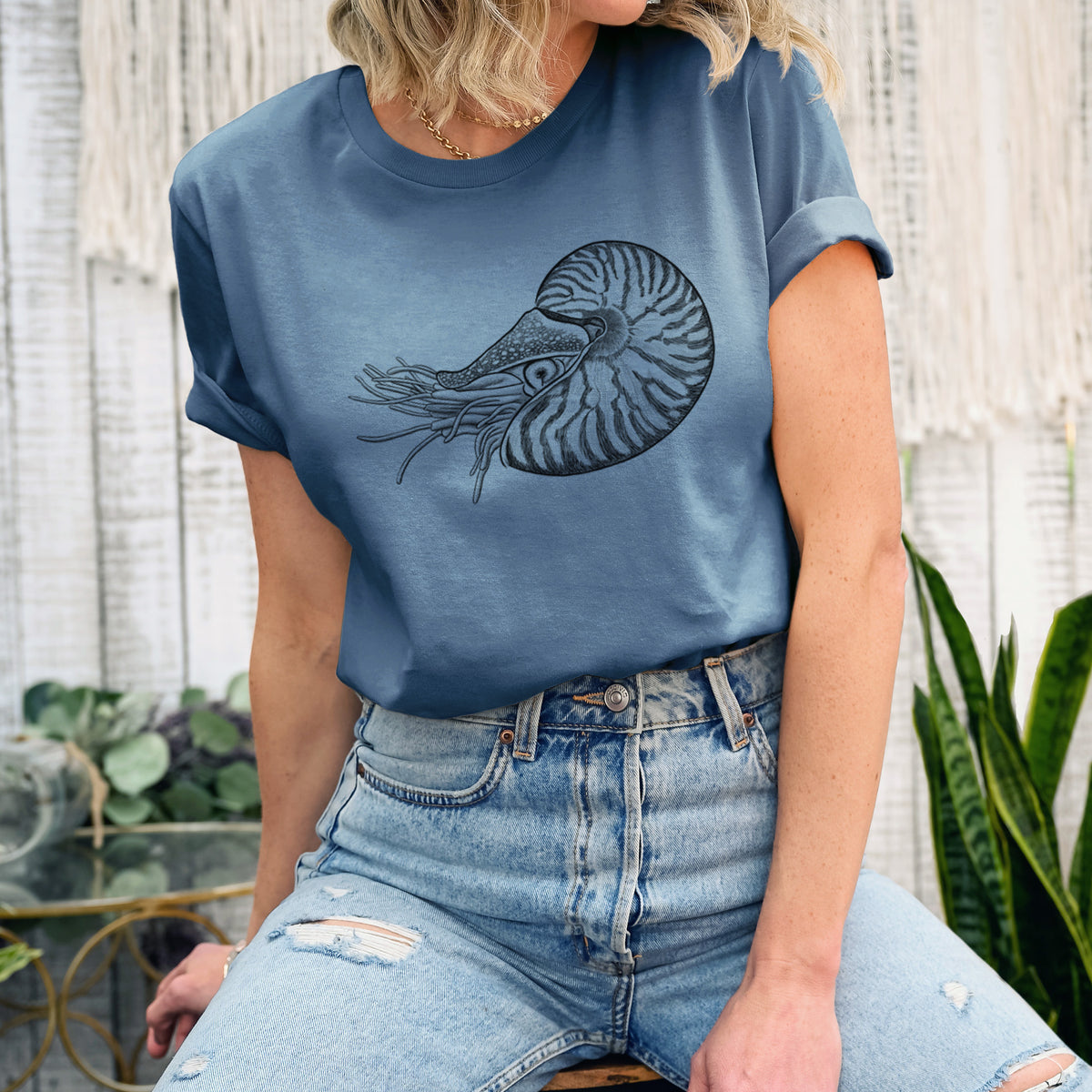 Woman wearing a steel blue lightweight cotton t-shirt printed with a detailed black ink illustration of a chambered nautilus with its striped spiral shell and tentacles.