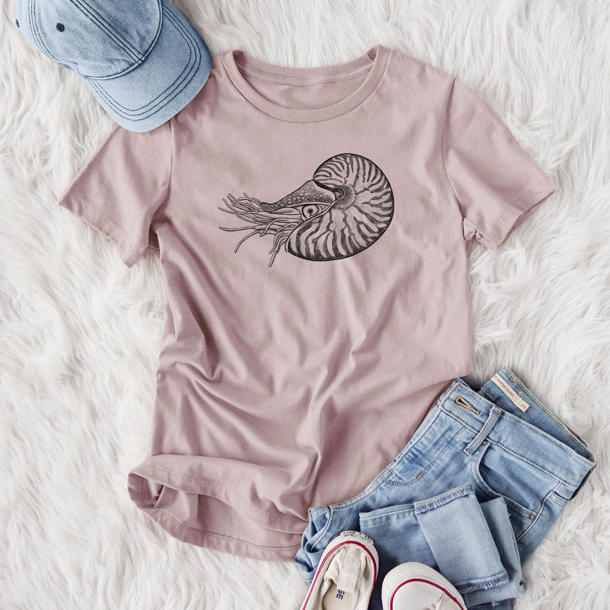 Women's relaxed fit cotton t-shirt printed with a detailed black ink illustration of a chambered nautilus with its striped spiral shell and tentacles, styled flat on a white faux fur rug with jeans.
