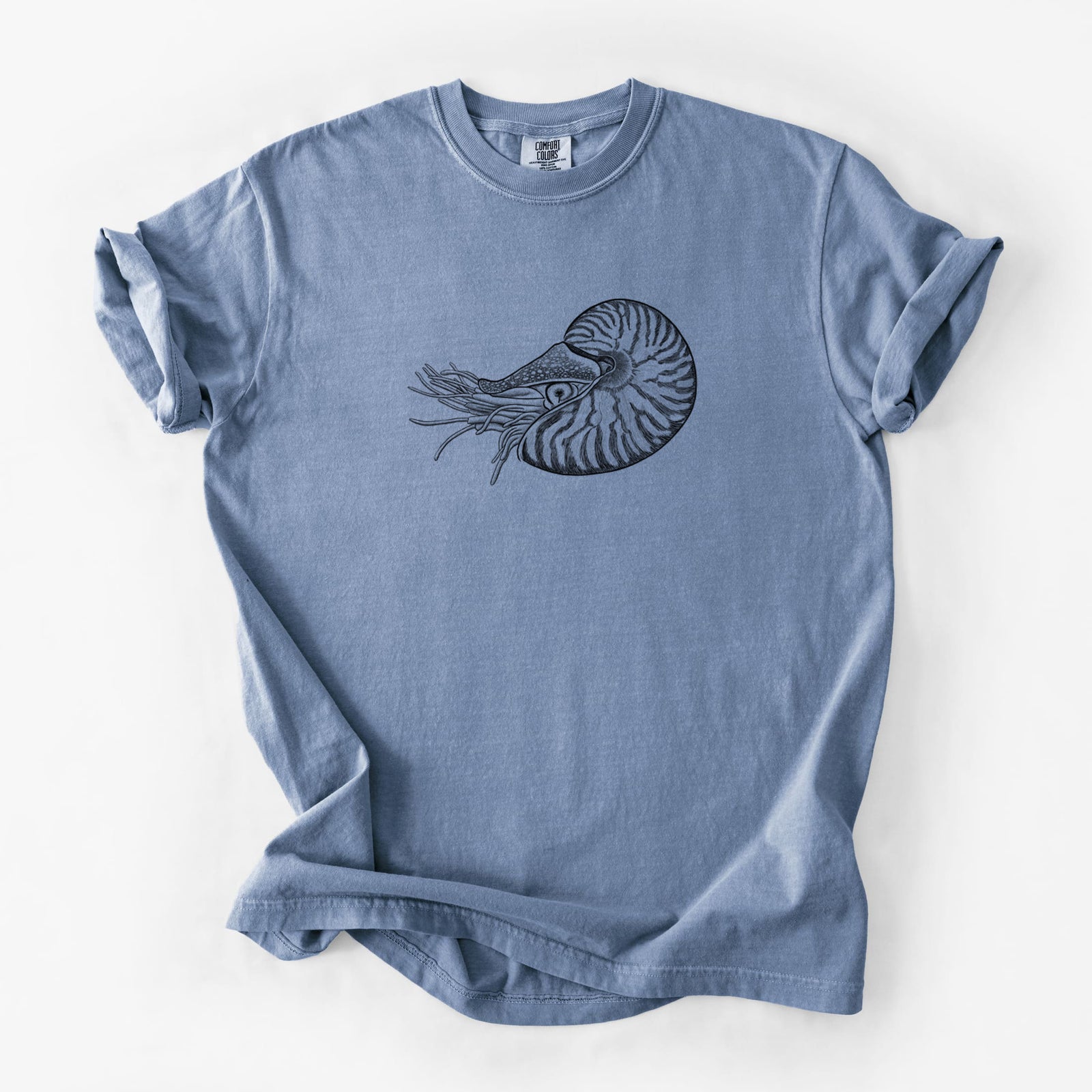 Blue jean Comfort Colors t-shirt laid flat, printed with a detailed black ink illustration of a chambered nautilus with its striped spiral shell and tentacles.