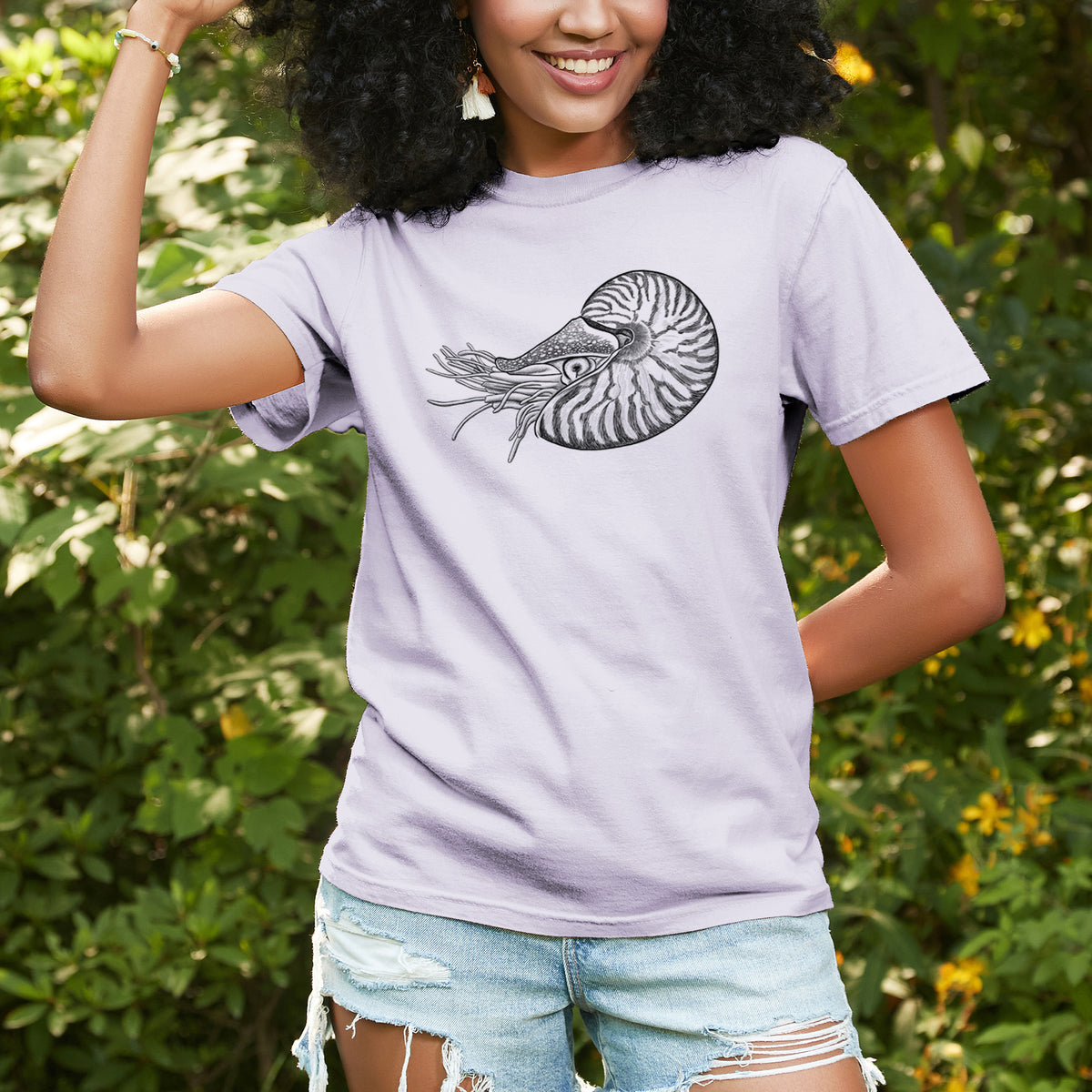 Woman wearing a Comfort Colors t-shirt printed with a detailed black ink illustration of a chambered nautilus with its striped spiral shell and tentacles, outdoors.