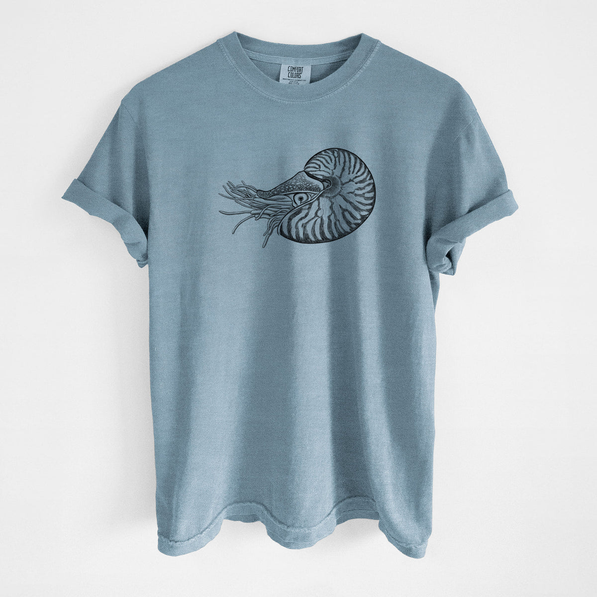 Steel blue Comfort Colors t-shirt laid flat, printed with a detailed black ink illustration of a chambered nautilus with its striped spiral shell and tentacles.