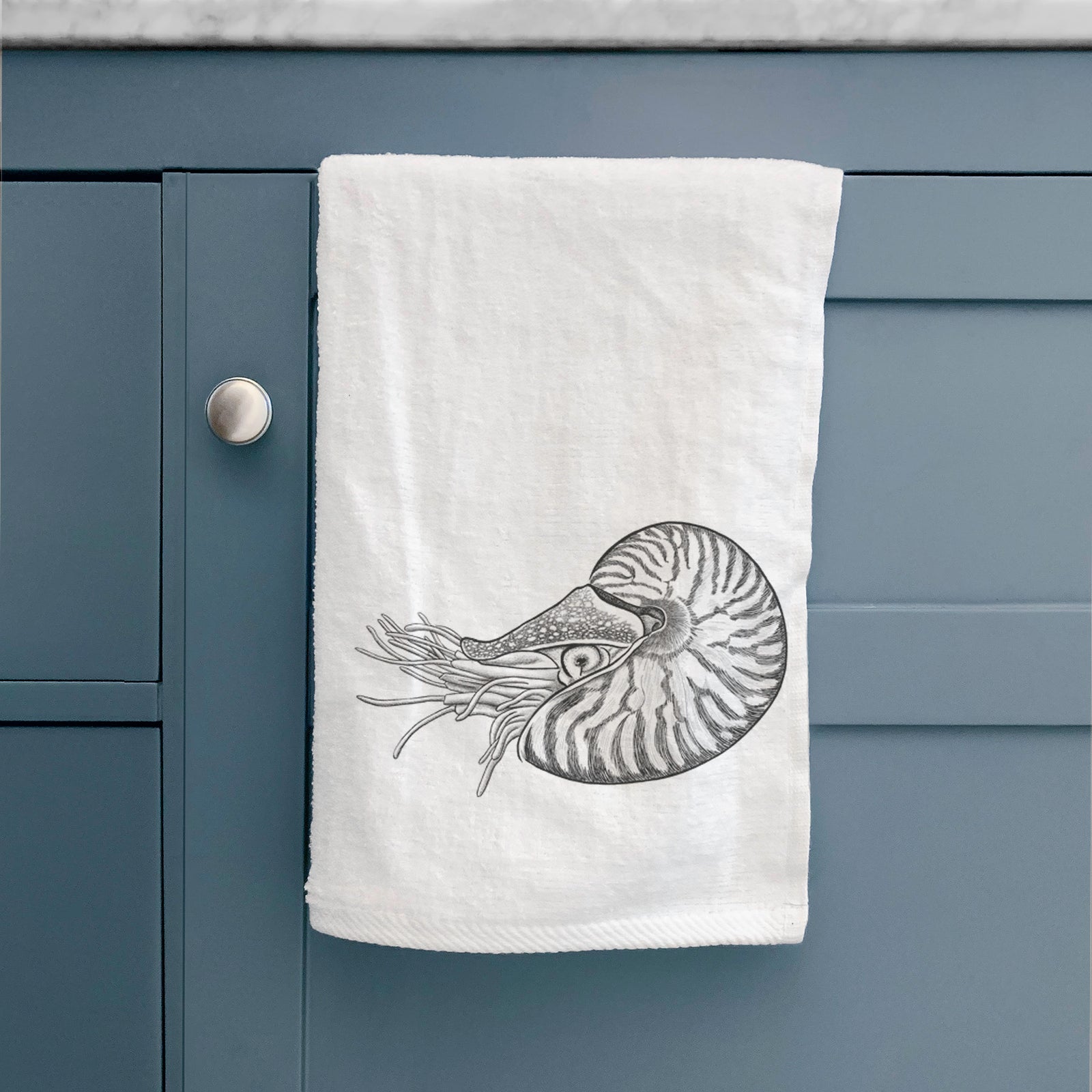 White hand towel printed with a detailed black ink illustration of a chambered nautilus with its striped spiral shell and tentacles.