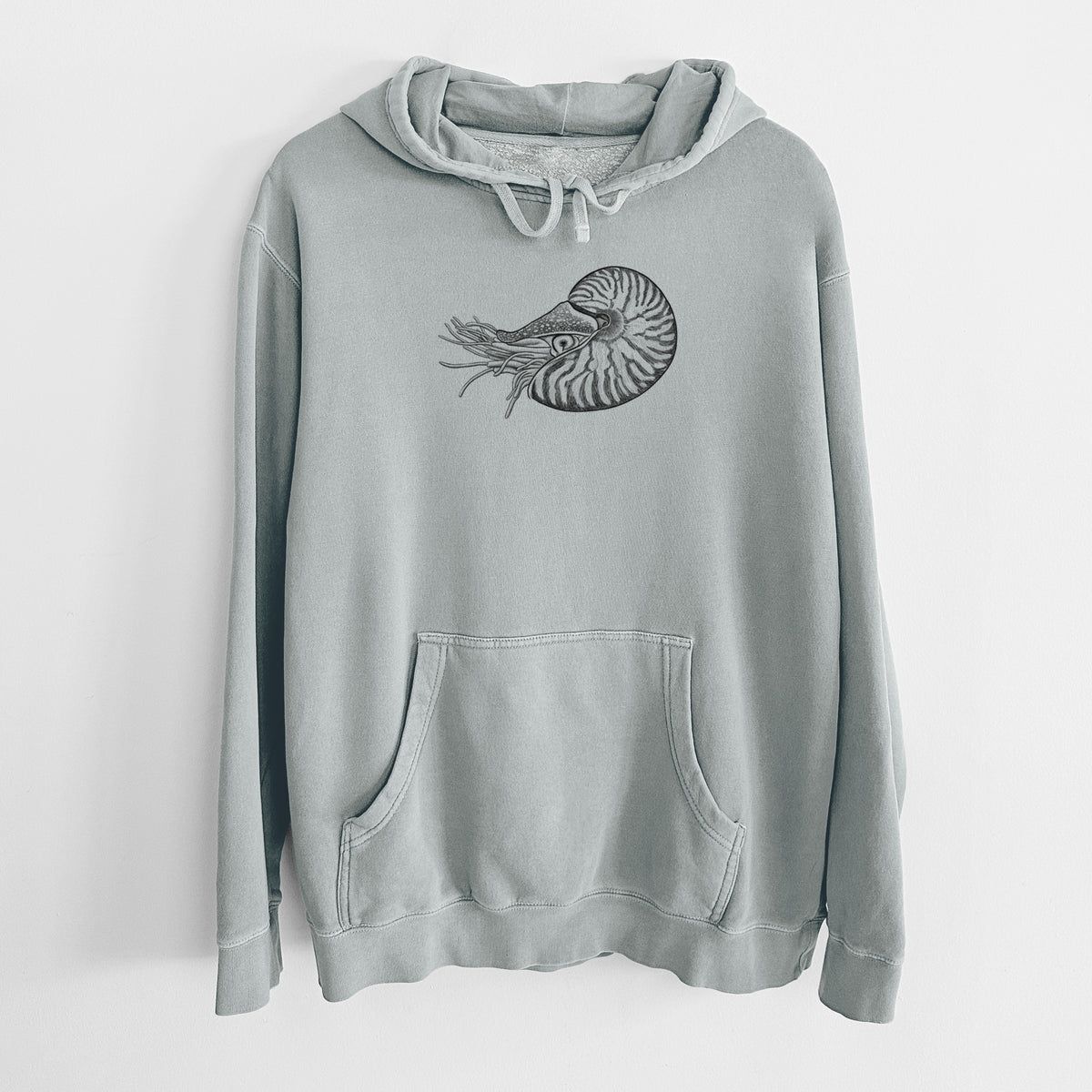Sage green pigment dyed hoodie laid flat, printed with a detailed black ink illustration of a chambered nautilus with its striped spiral shell and tentacles.