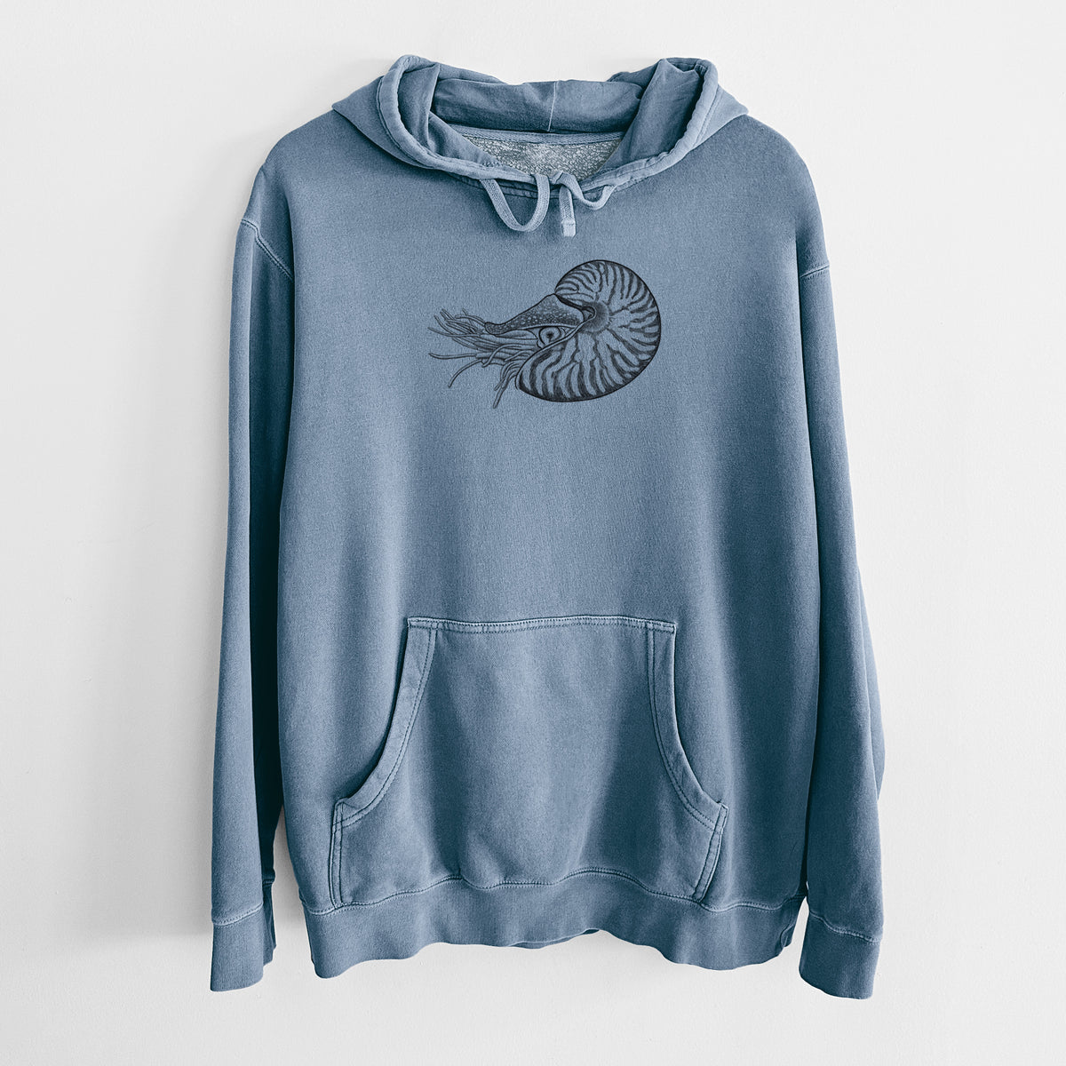 Slate blue pigment dyed hoodie laid flat, printed with a detailed black ink illustration of a chambered nautilus with its striped spiral shell and tentacles.