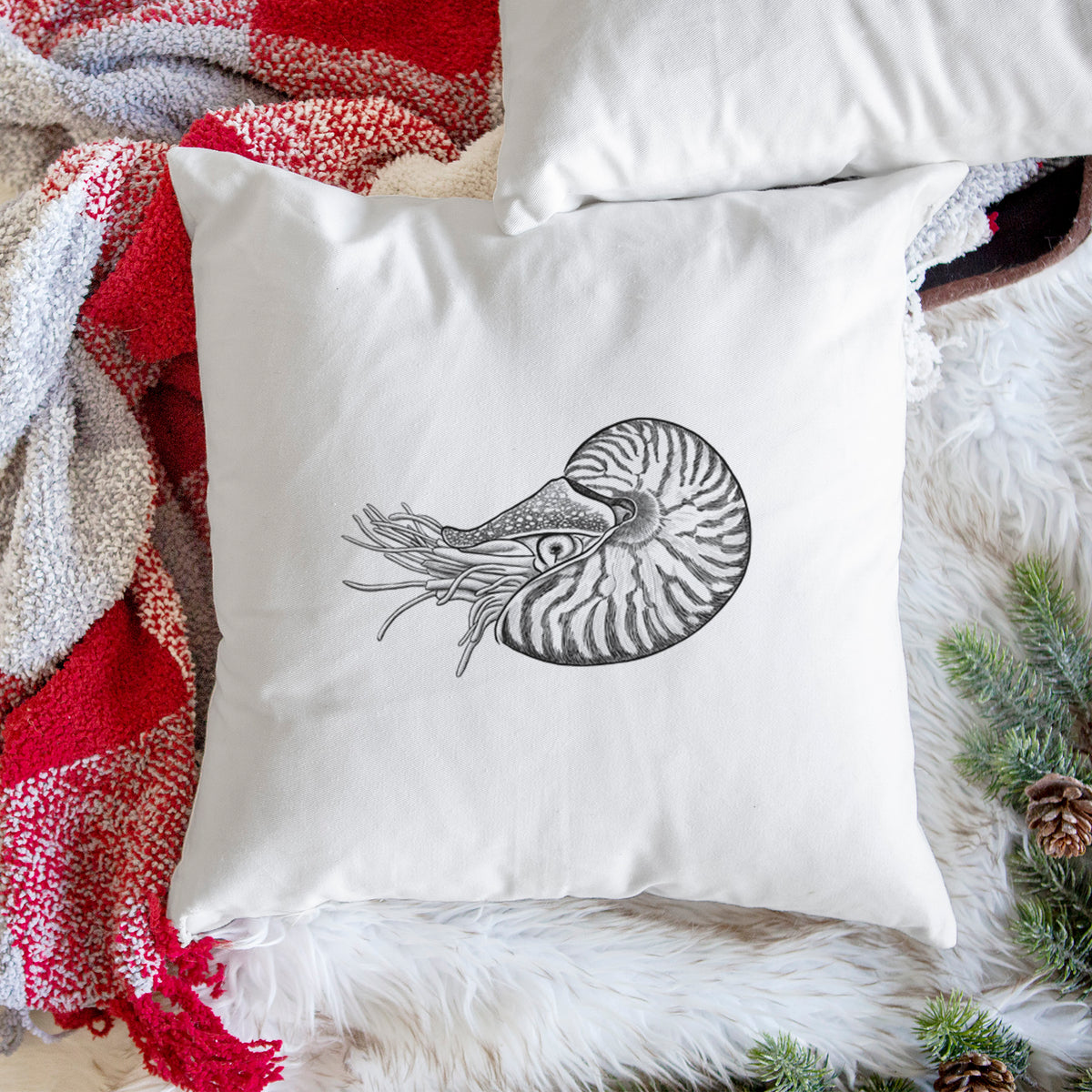 White pillow cover printed with a detailed black ink illustration of a chambered nautilus with its striped spiral shell and tentacles, on a woven chair.