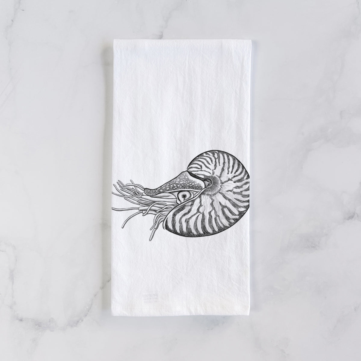 White cotton tea towel laid flat on marble, printed with a detailed black ink illustration of a chambered nautilus with its striped spiral shell and tentacles.