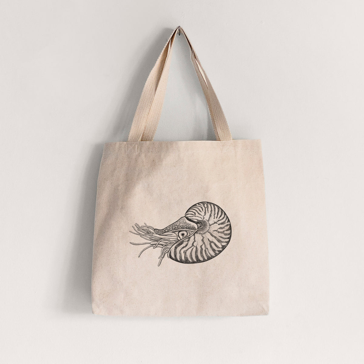 Natural canvas tote bag printed with a detailed black ink illustration of a chambered nautilus with its striped spiral shell and tentacles.