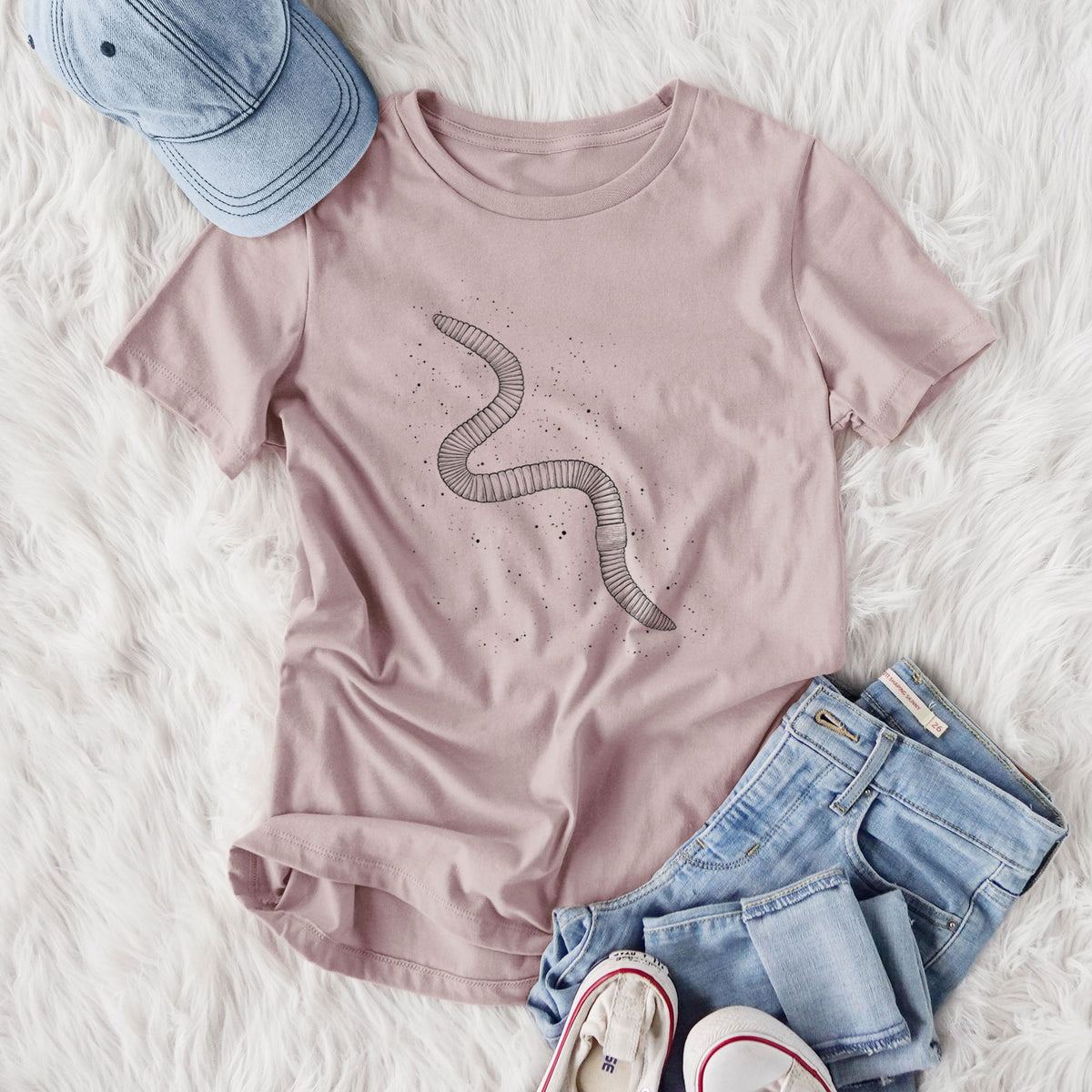 Women's relaxed fit cotton t-shirt printed with a black ink illustration of a nightcrawler earthworm with soil specks, styled flat on a white faux fur rug with jeans.