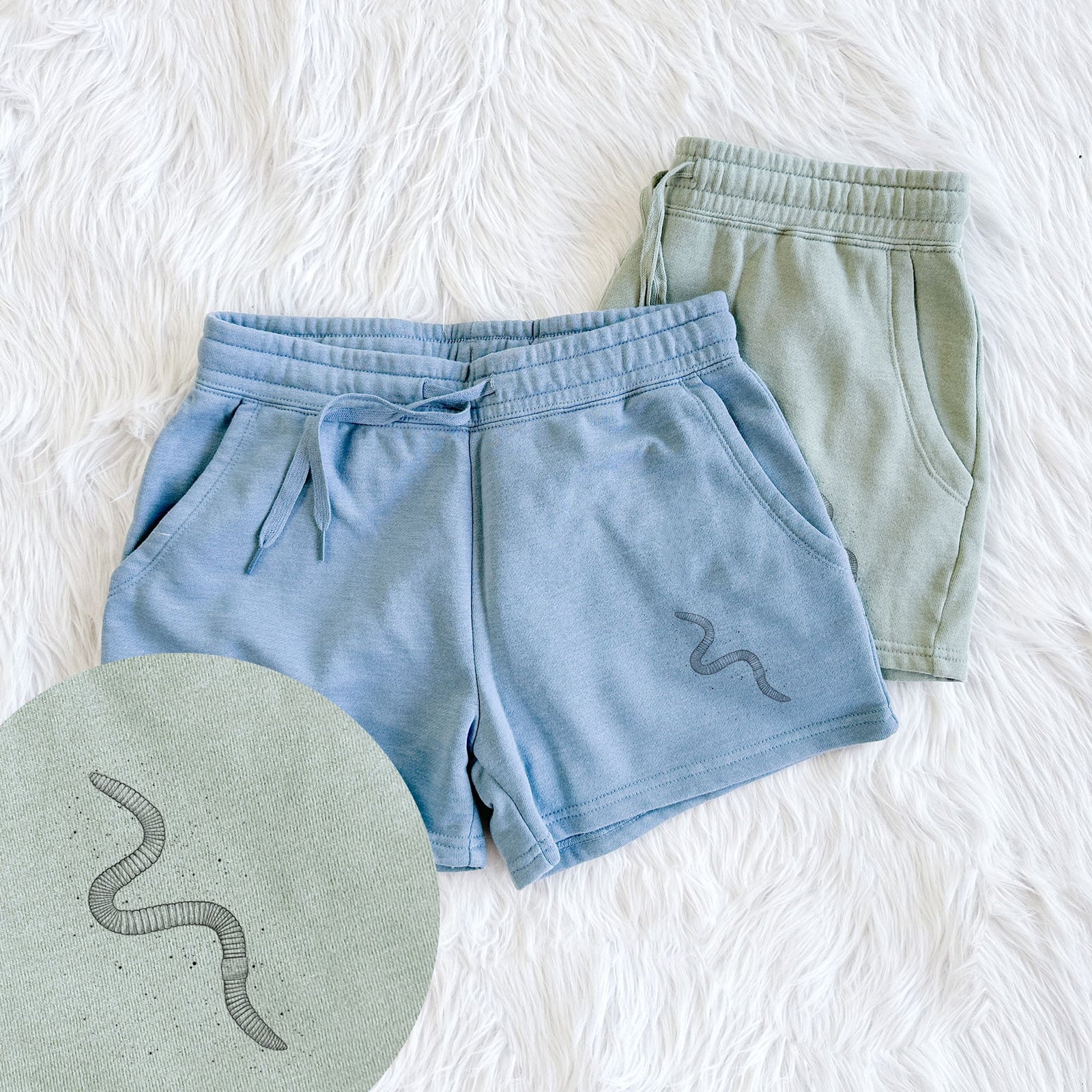Two pairs of Cali Wave shorts in different colors printed with a black ink illustration of a nightcrawler earthworm with soil specks, with a close-up of the print.