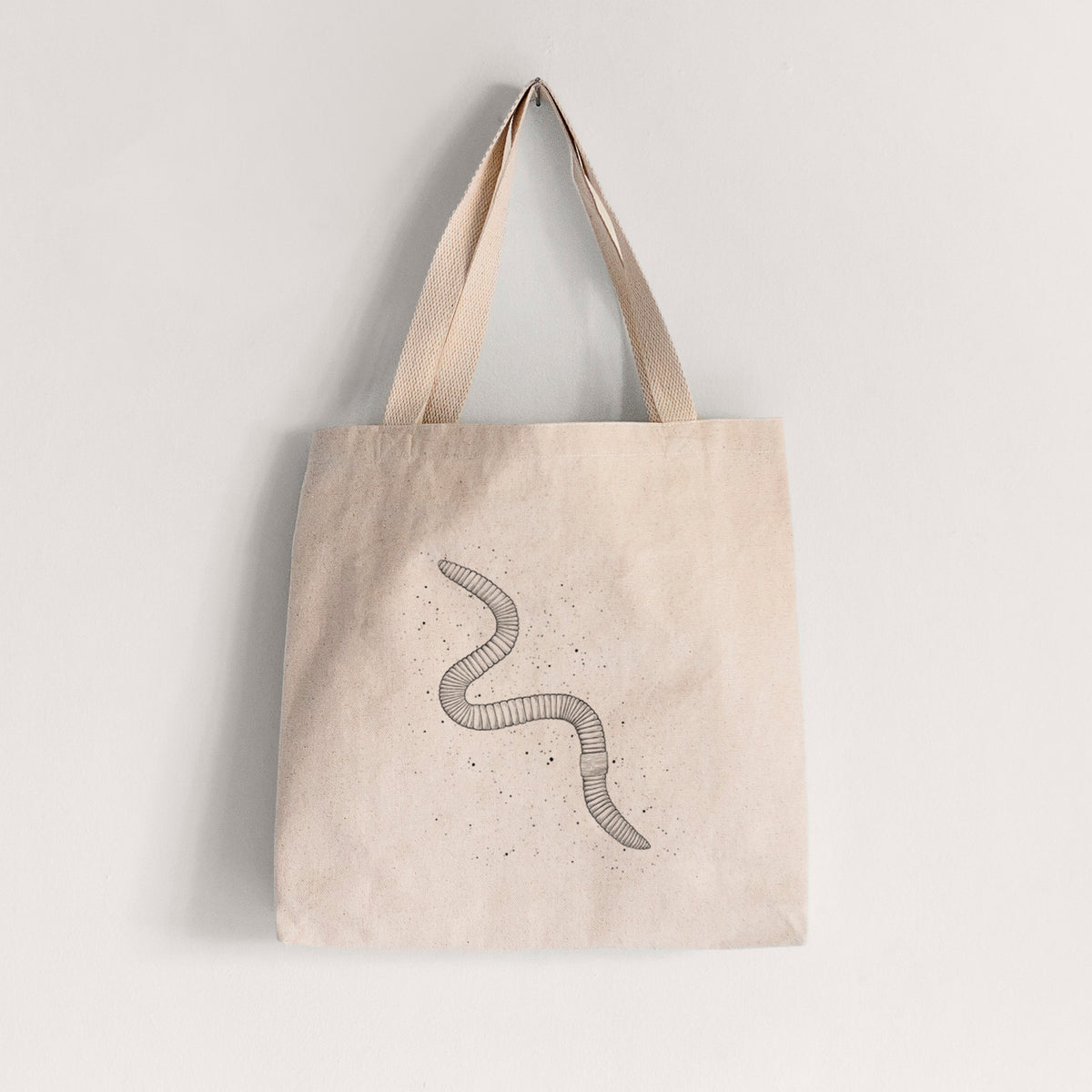 Natural canvas tote bag printed with a black ink illustration of a nightcrawler earthworm with soil specks.