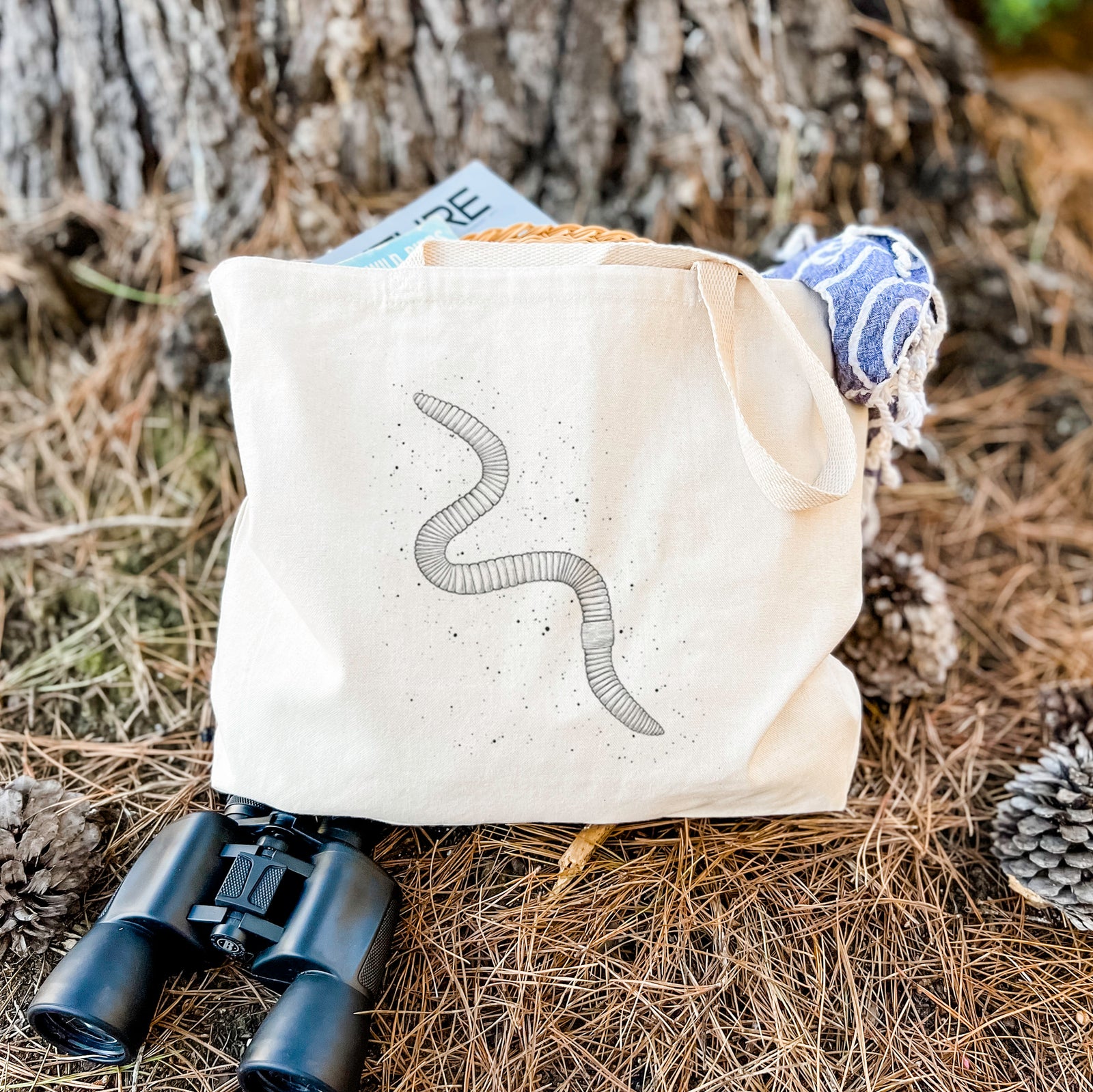 Natural canvas tote bag printed with a black ink illustration of a nightcrawler earthworm with soil specks.