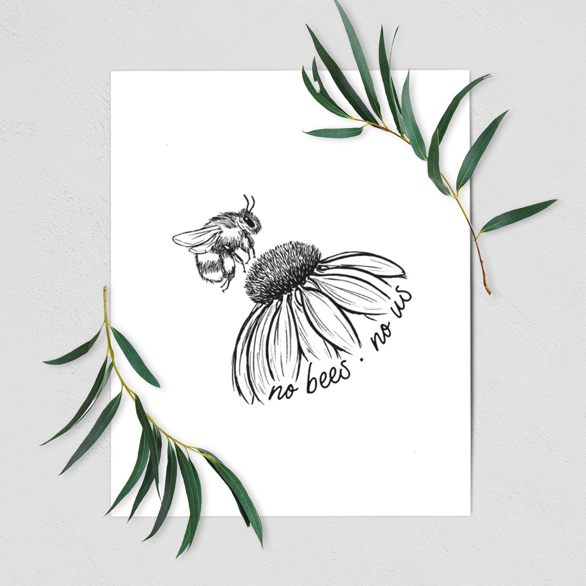 Art print of a black ink illustration of a bee flying toward a coneflower, with the handwritten words no bees no us, shown with eucalyptus leaves.