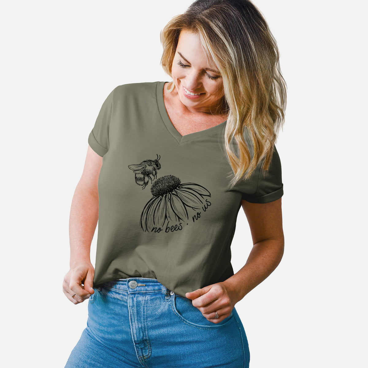 Woman wearing a military green women's relaxed fit cotton V-neck t-shirt printed with a black ink illustration of a bee flying toward a coneflower, with the handwritten words no bees no us.