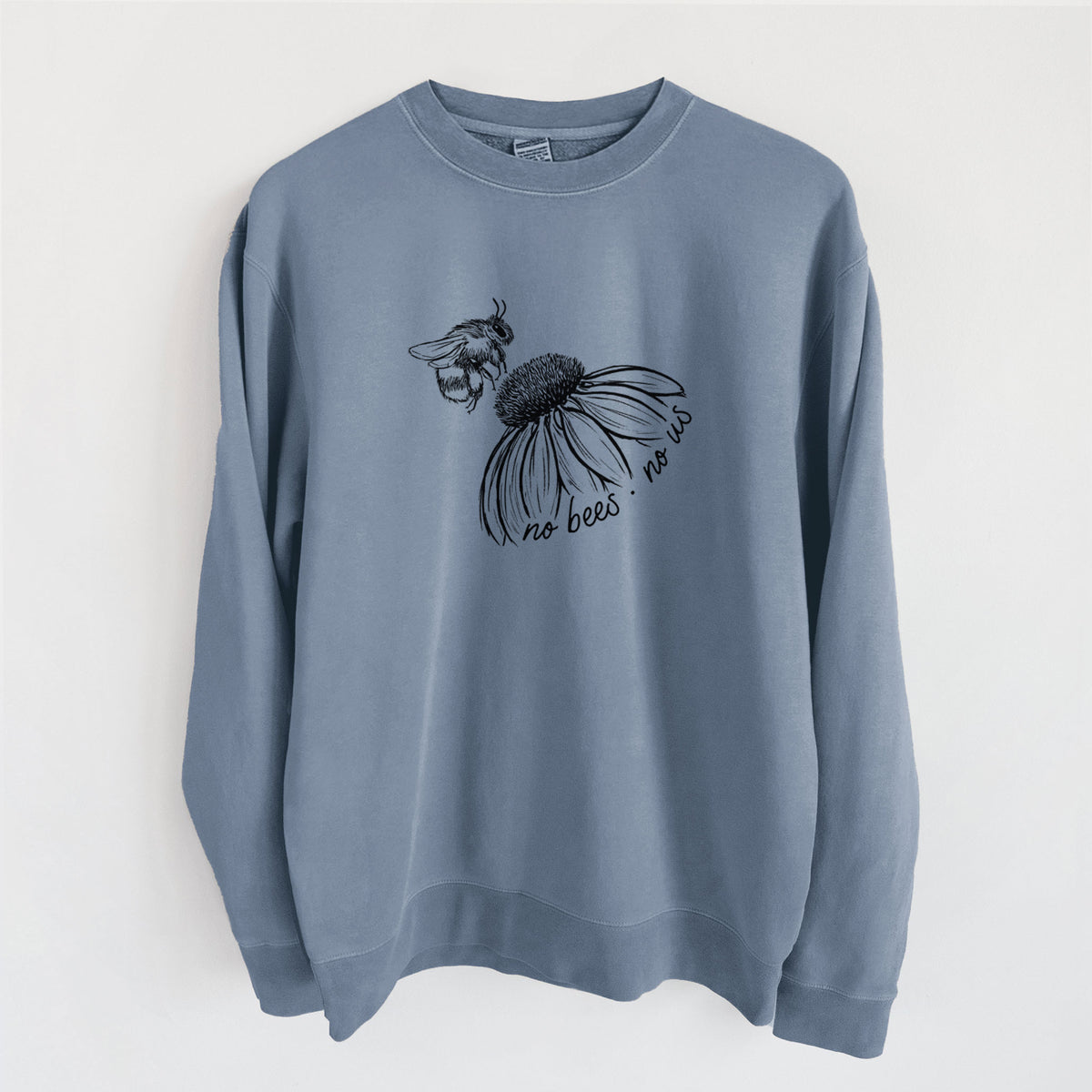 Slate blue pigment dyed crewneck sweatshirt laid flat, printed with a black ink illustration of a bee flying toward a coneflower, with the handwritten words no bees no us.