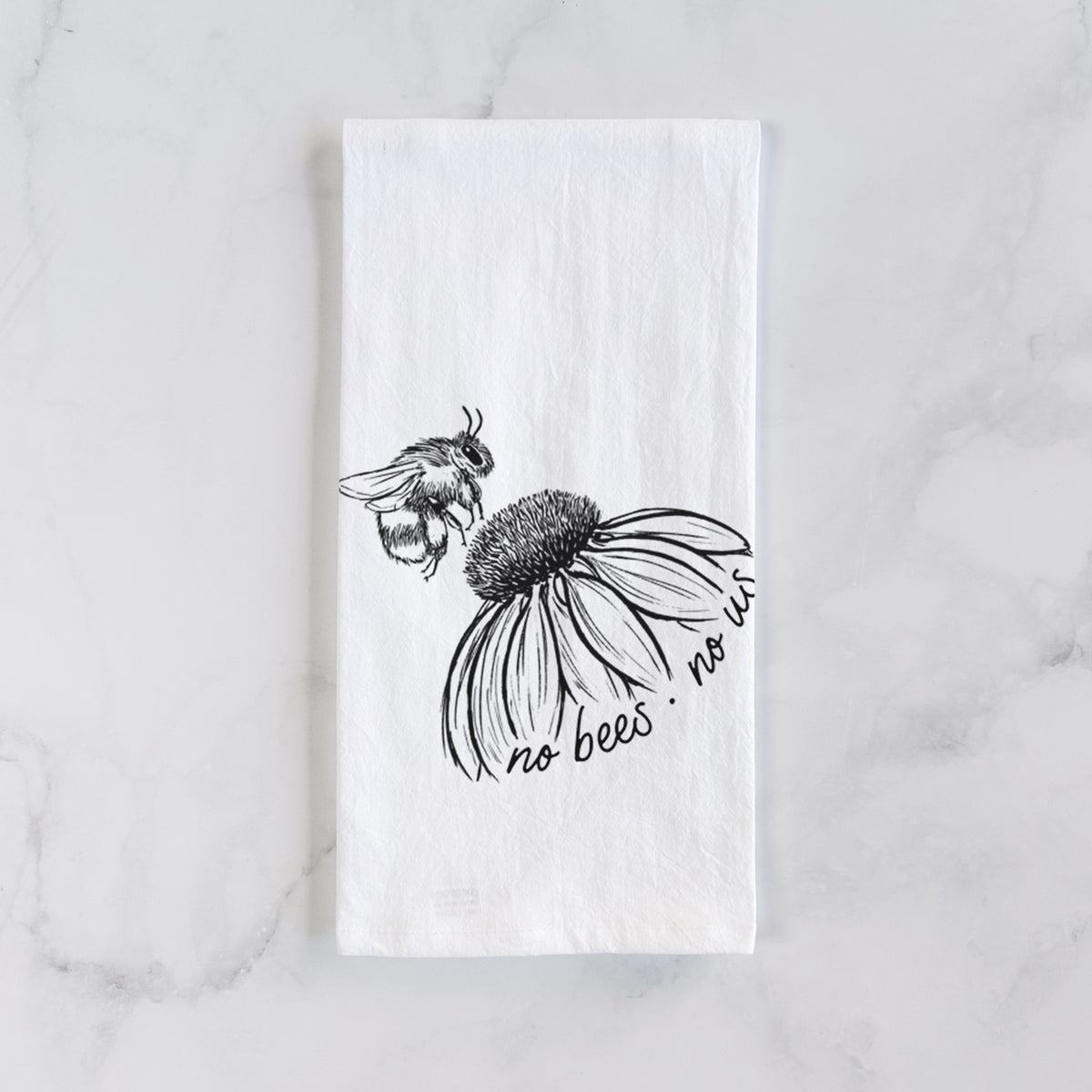 White cotton tea towel laid flat on marble, printed with a black ink illustration of a bee flying toward a coneflower, with the handwritten words no bees no us.