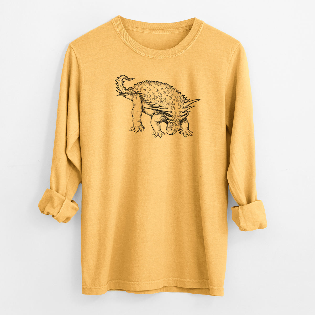 Golden wheat yellow Comfort Colors long sleeve shirt laid flat with the cuffs rolled, printed with a black ink illustration of an armored Nodosaurus.