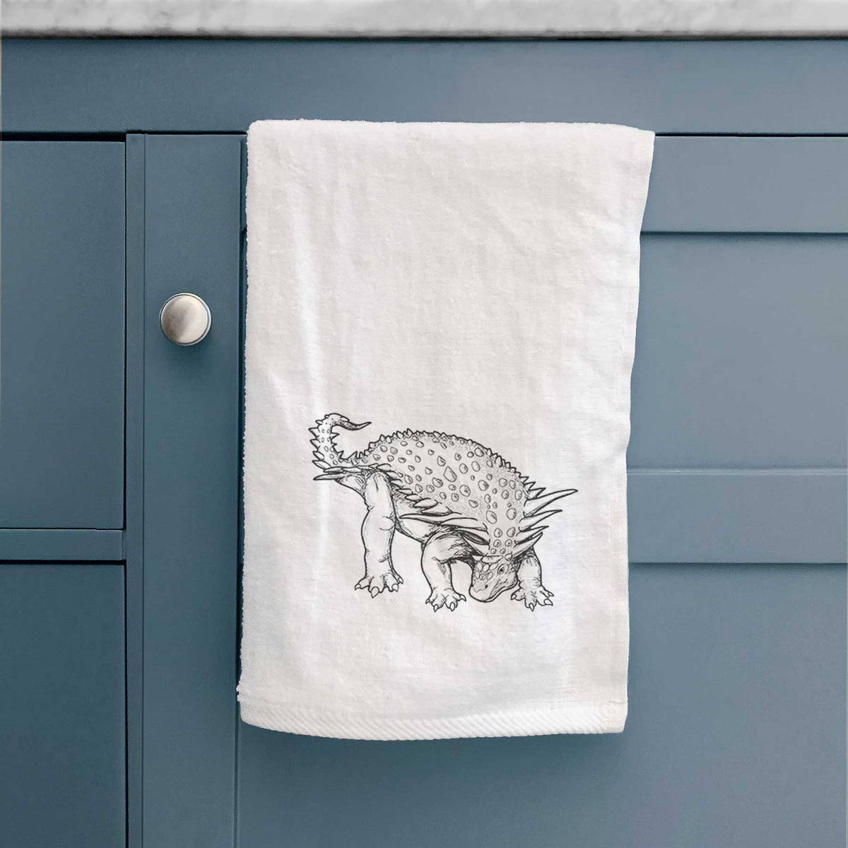 White hand towel printed with a black ink illustration of an armored Nodosaurus.