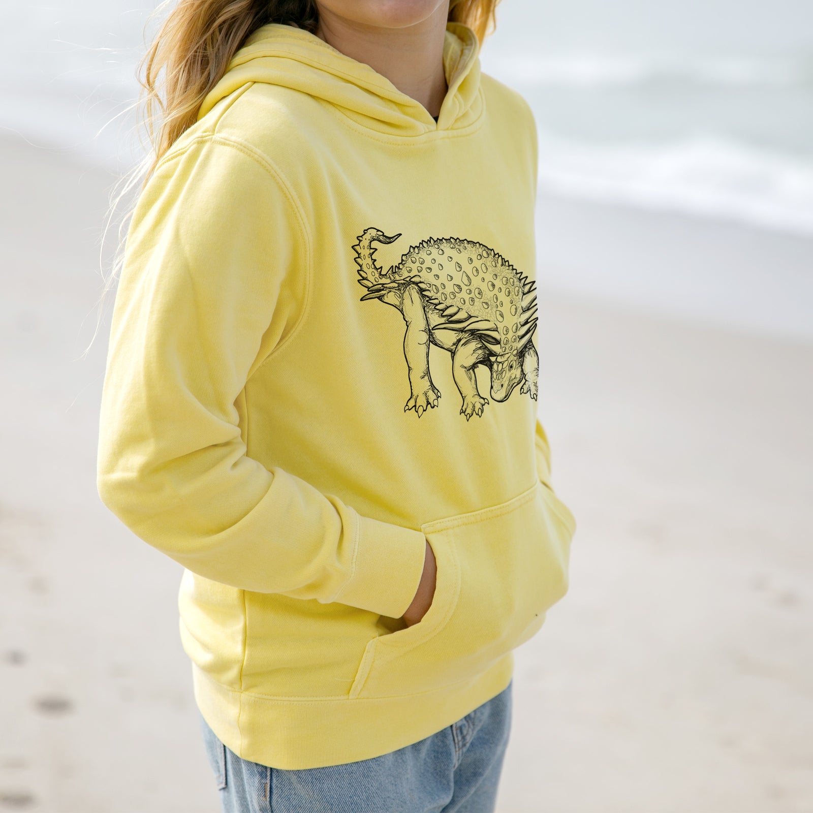 Boy wearing a youth pigment dyed hoodie printed with a black ink illustration of an armored Nodosaurus.