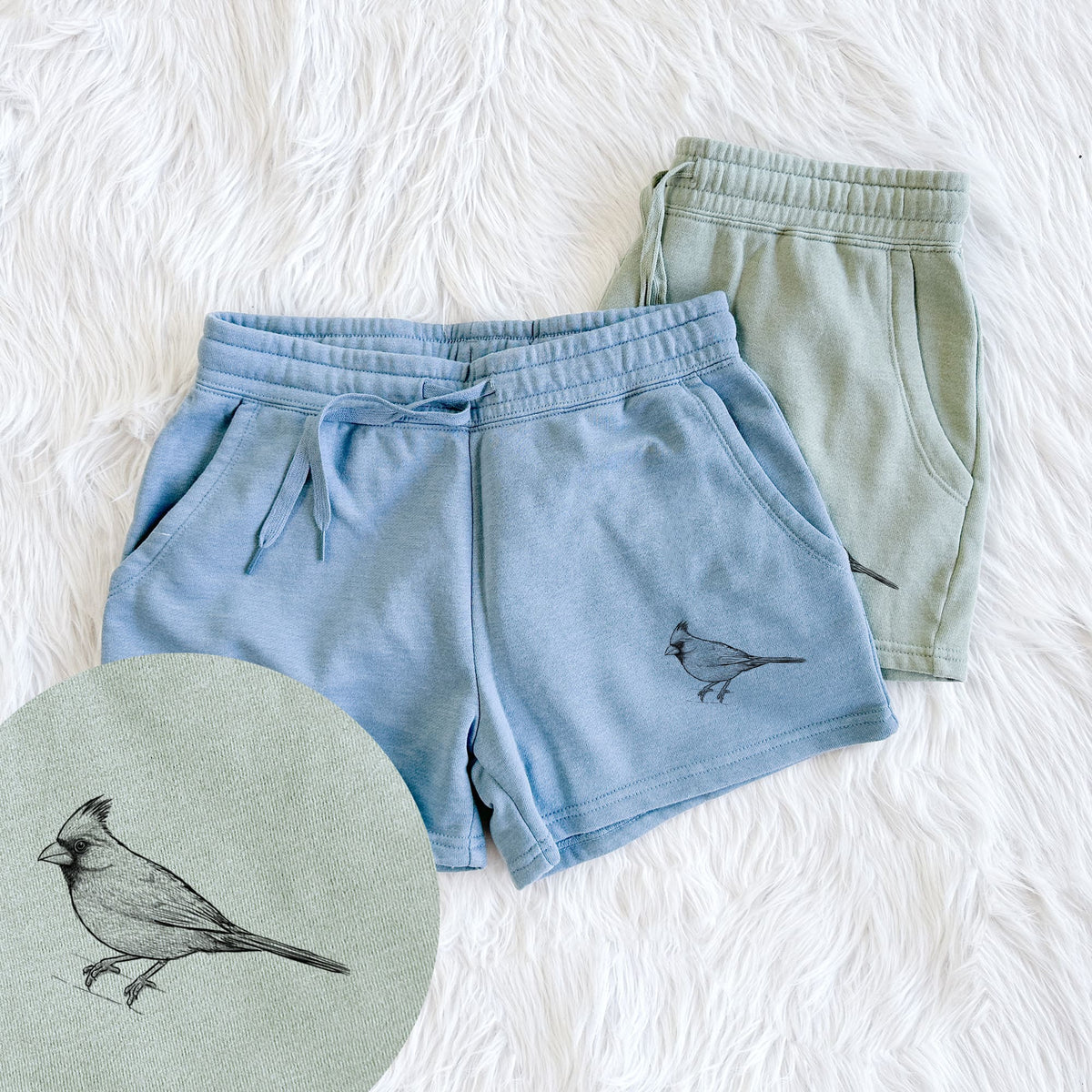 Two pairs of Cali Wave shorts in different colors printed with a detailed black ink sketch of a northern cardinal perched with its crest raised, with a close-up of the print.