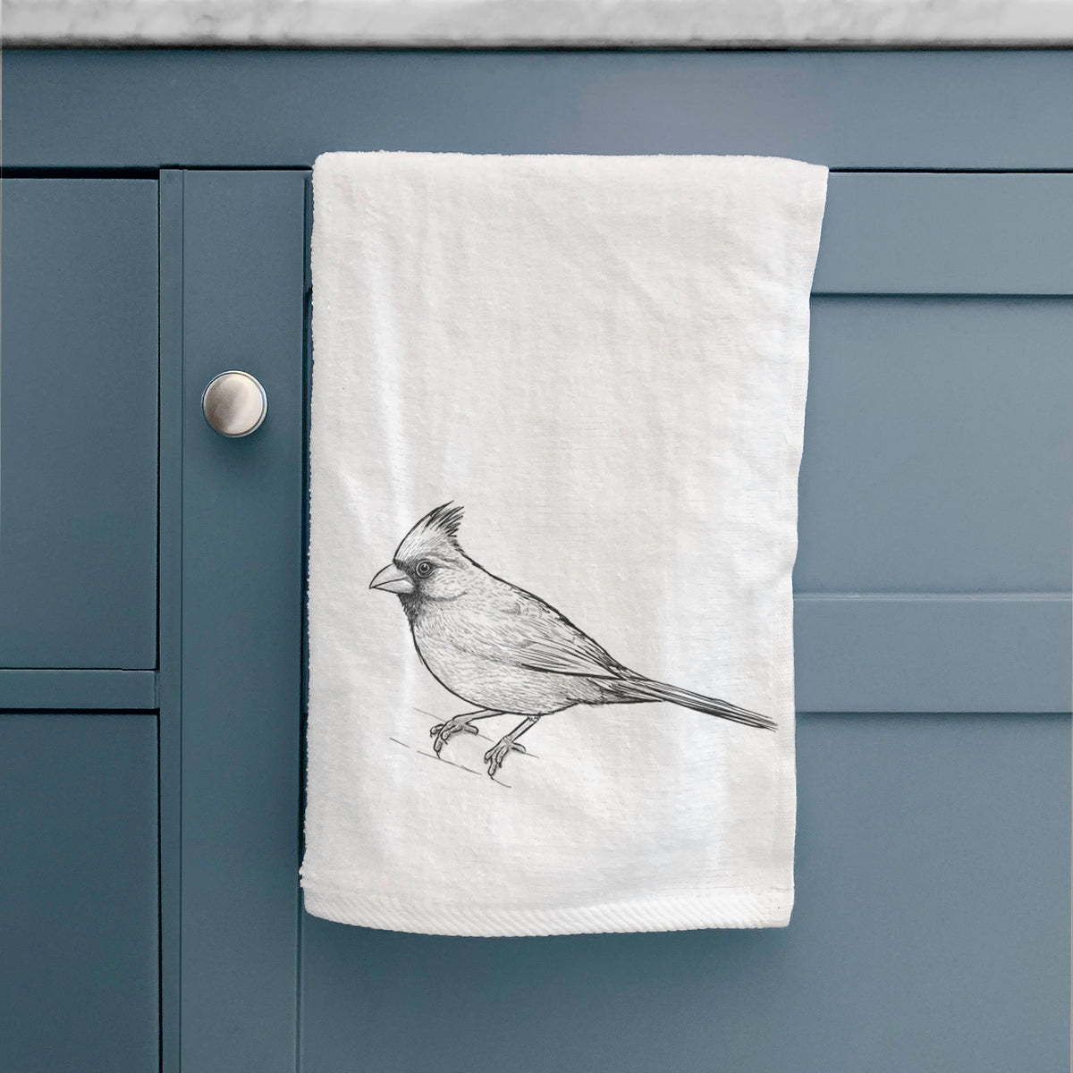 White hand towel printed with a detailed black ink sketch of a northern cardinal perched with its crest raised, hanging on a cabinet door.