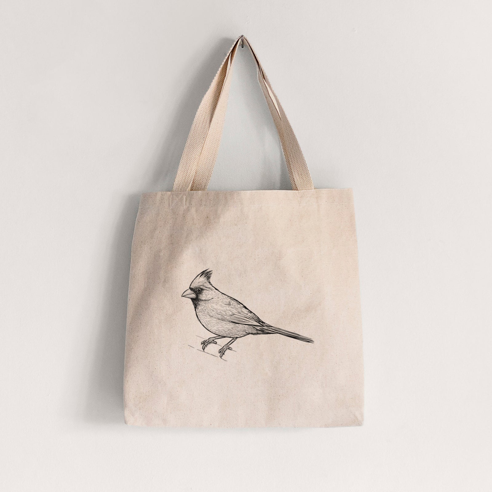 Natural canvas tote bag printed with a detailed black ink sketch of a northern cardinal perched with its crest raised.
