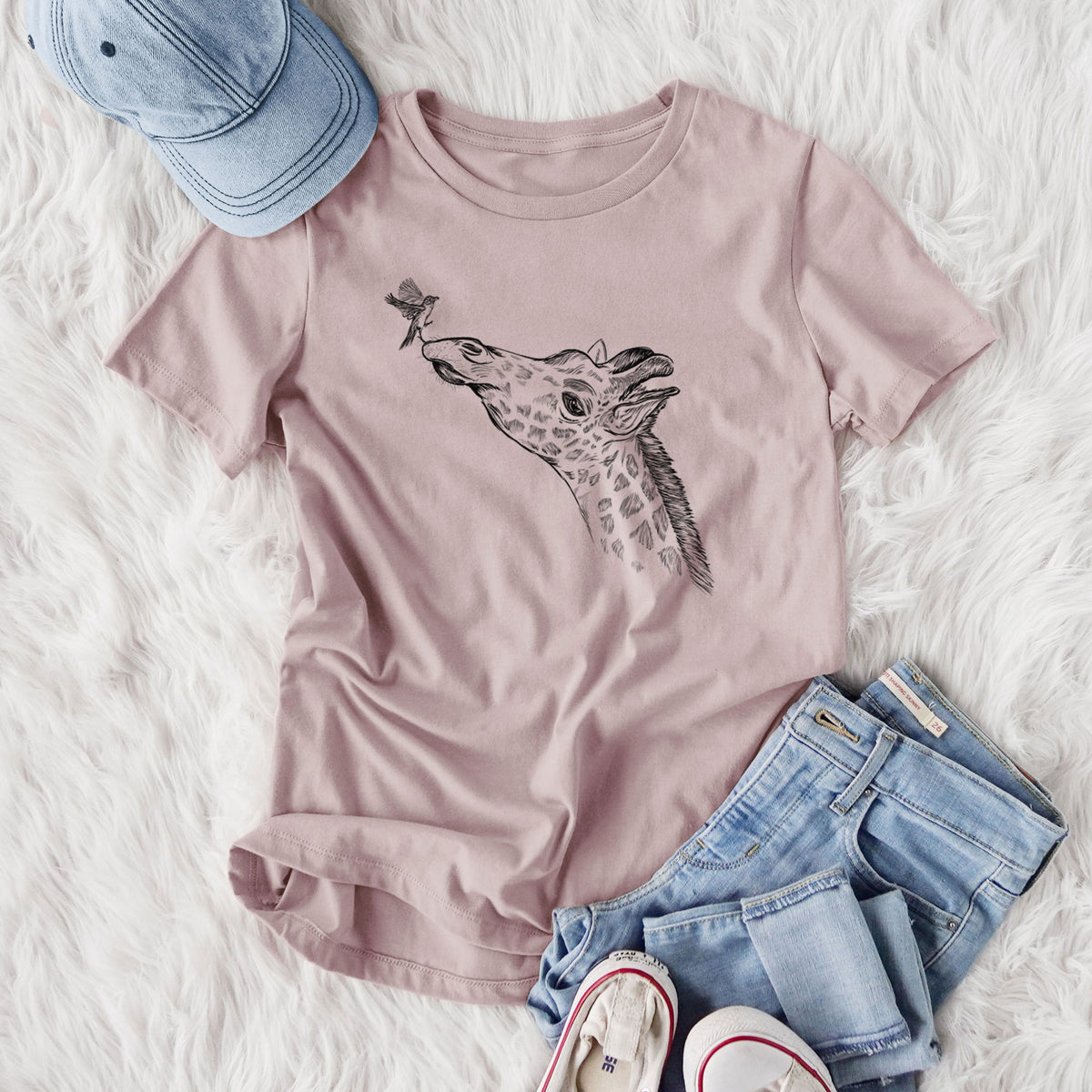Women's relaxed fit cotton t-shirt printed with a black ink illustration of a northern giraffe reaching its head up to nibble a flower, styled flat on a white faux fur rug with jeans.