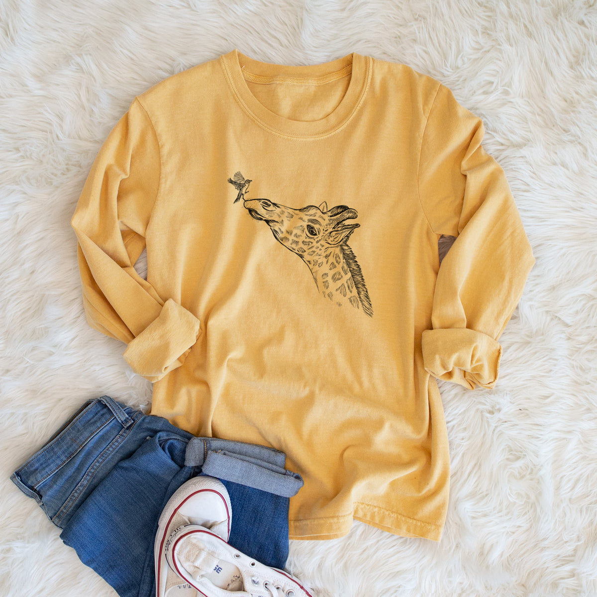 Golden wheat yellow Comfort Colors long sleeve shirt printed with a black ink illustration of a northern giraffe reaching its head up to nibble a flower, shown in a lifestyle photo.