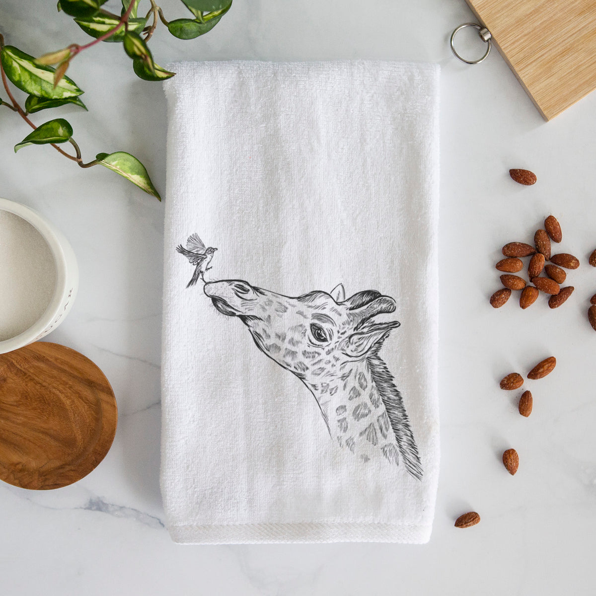 White hand towel printed with a black ink illustration of a northern giraffe reaching its head up to nibble a flower.