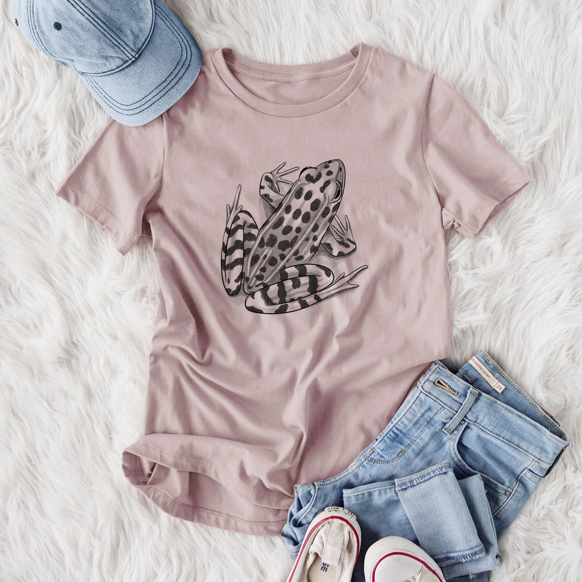 Women's relaxed fit cotton t-shirt printed with a detailed black ink illustration of a spotted northern leopard frog, styled flat on a white faux fur rug with jeans.