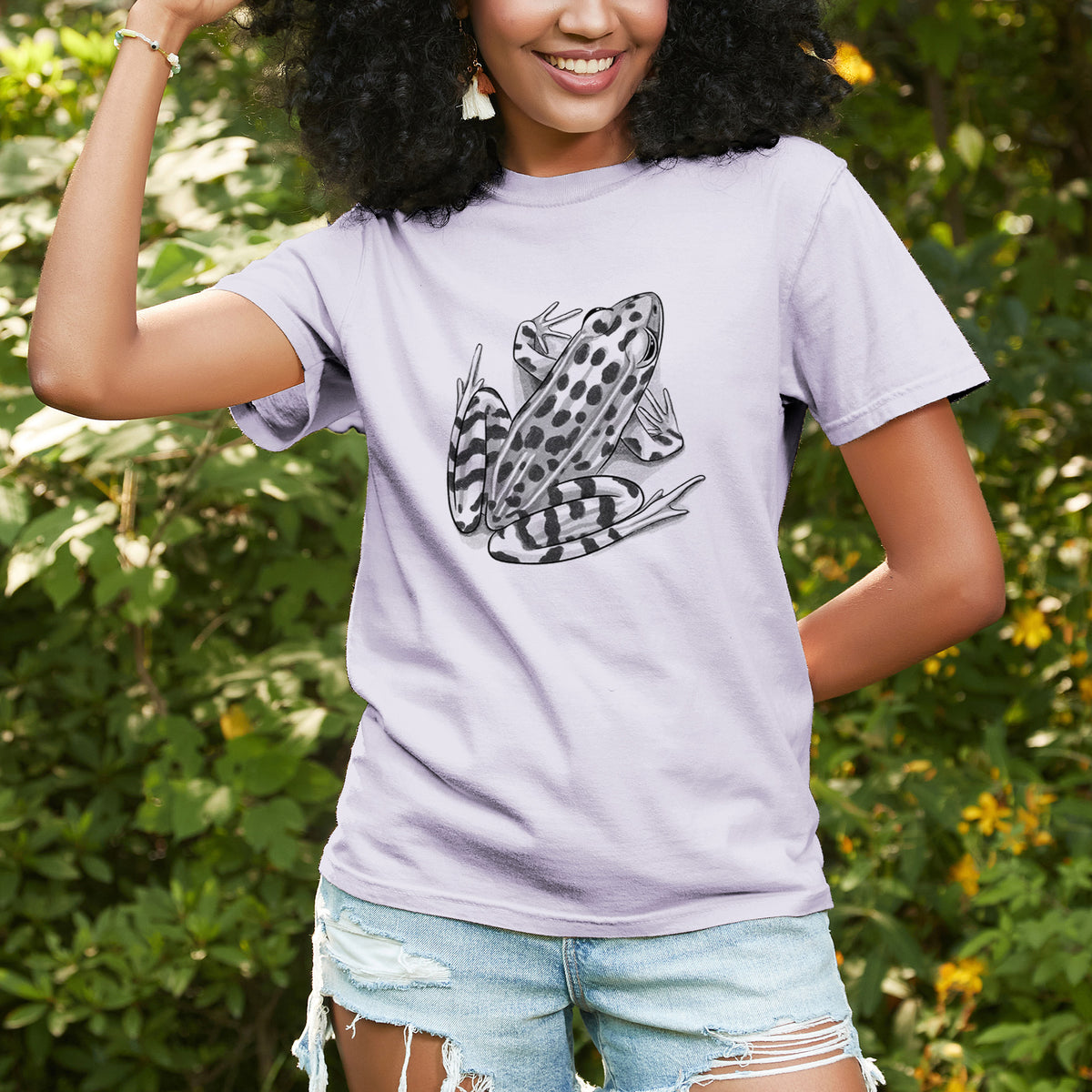 Woman wearing a Comfort Colors t-shirt printed with a detailed black ink illustration of a spotted northern leopard frog, outdoors.