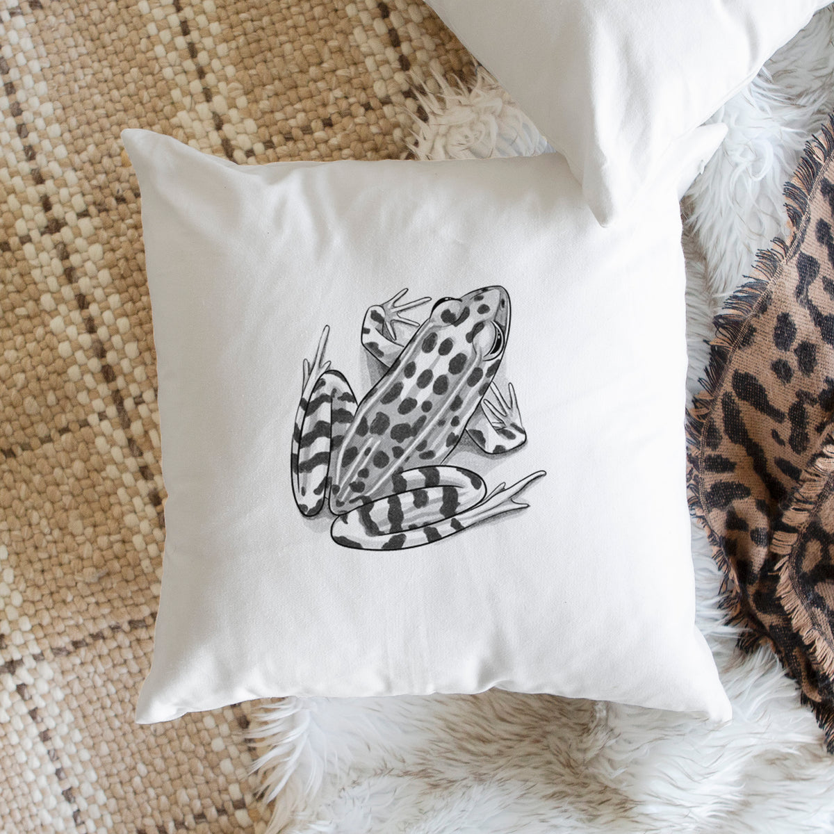 White pillow cover printed with a detailed black ink illustration of a spotted northern leopard frog, on a woven chair.