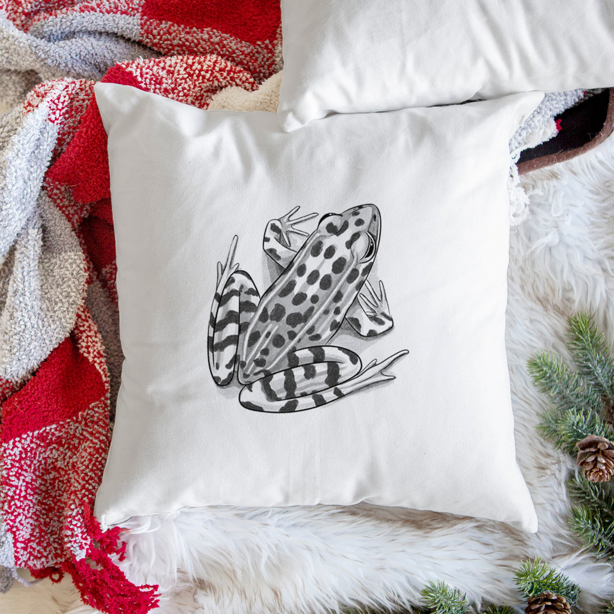 White pillow cover printed with a detailed black ink illustration of a spotted northern leopard frog, on a woven chair.