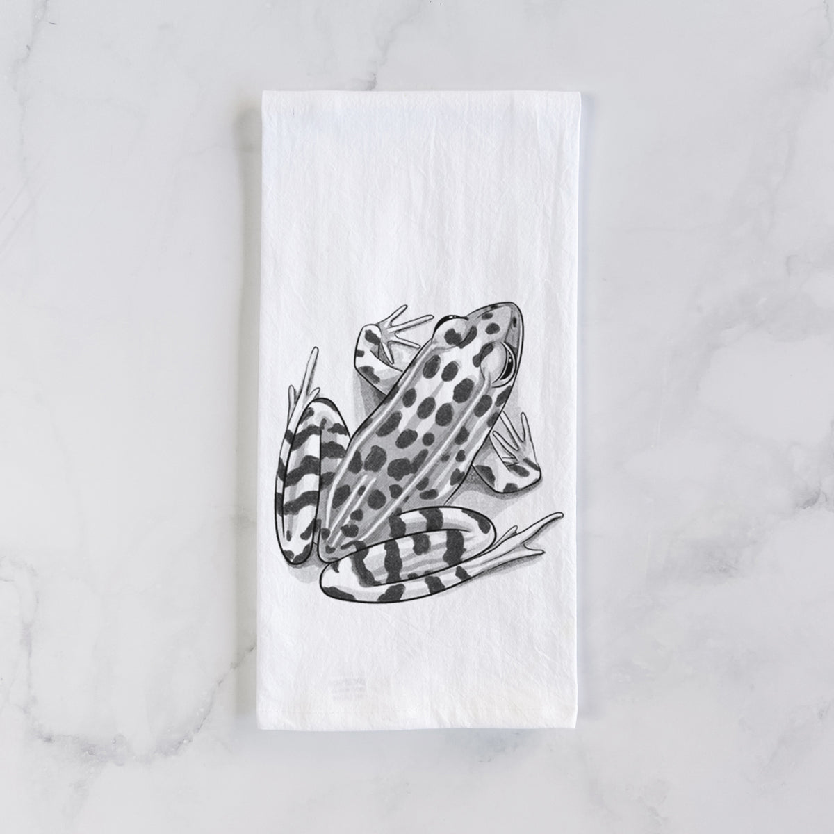 White cotton tea towel laid flat on marble, printed with a detailed black ink illustration of a spotted northern leopard frog.
