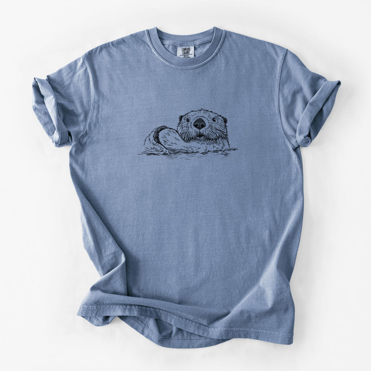 Blue jean Comfort Colors t-shirt laid flat, printed with a black ink illustration of a northern river otter peeking out of the water.