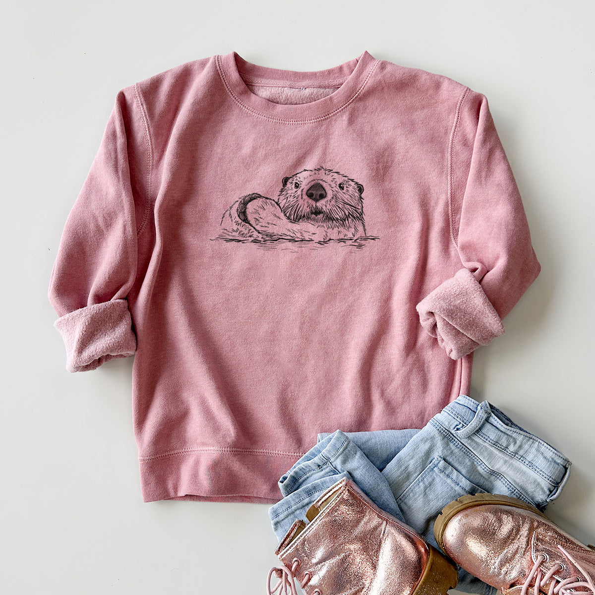 Youth crewneck sweatshirt printed with a black ink illustration of a northern river otter peeking out of the water, styled flat with jeans and boots.