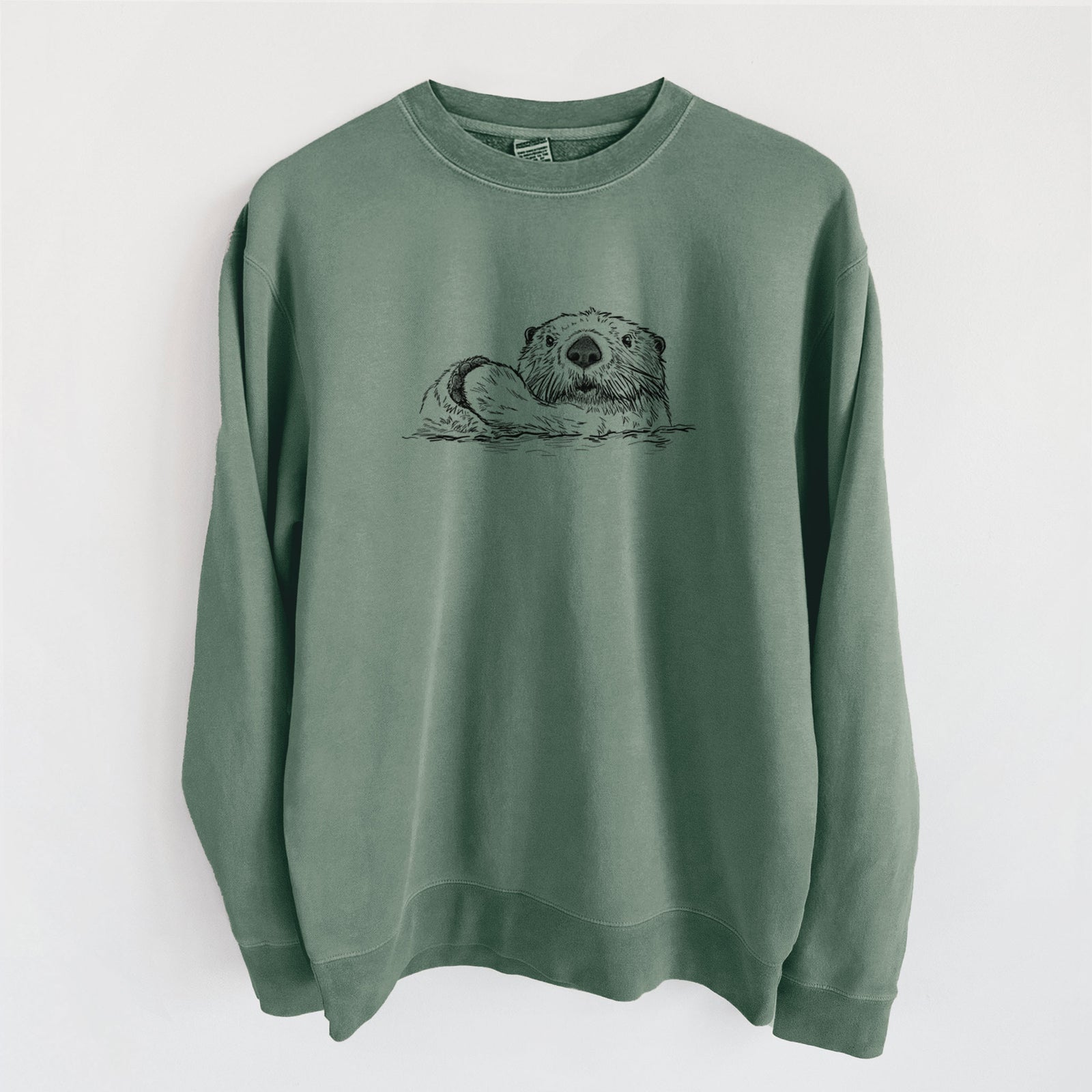 Alpine green pigment dyed crewneck sweatshirt laid flat, printed with a black ink illustration of a northern river otter peeking out of the water.