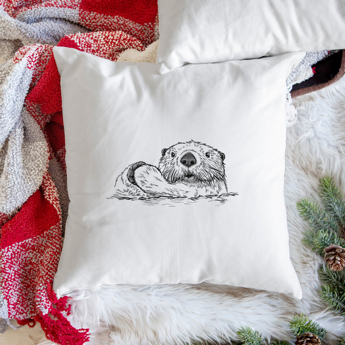 White pillow cover printed with a black ink illustration of a northern river otter peeking out of the water, on a woven chair.
